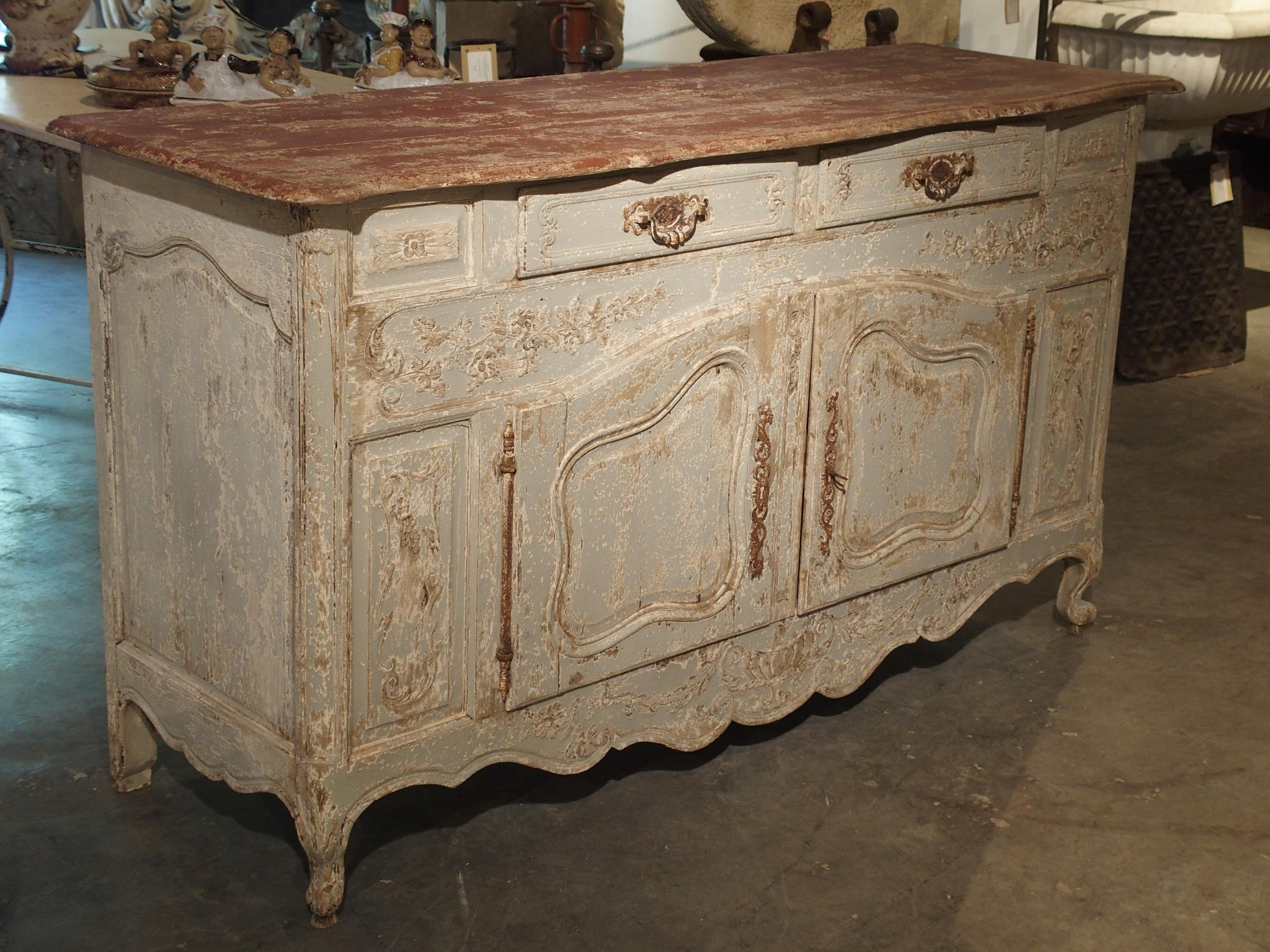 From Provence, this wonderful pale blue buffet has a brick red wooden top. There is a scalloped top with two center drawers directly beneath this. Two faux panels are on either side of the drawers. The floral and foliate frieze beneath has two doors