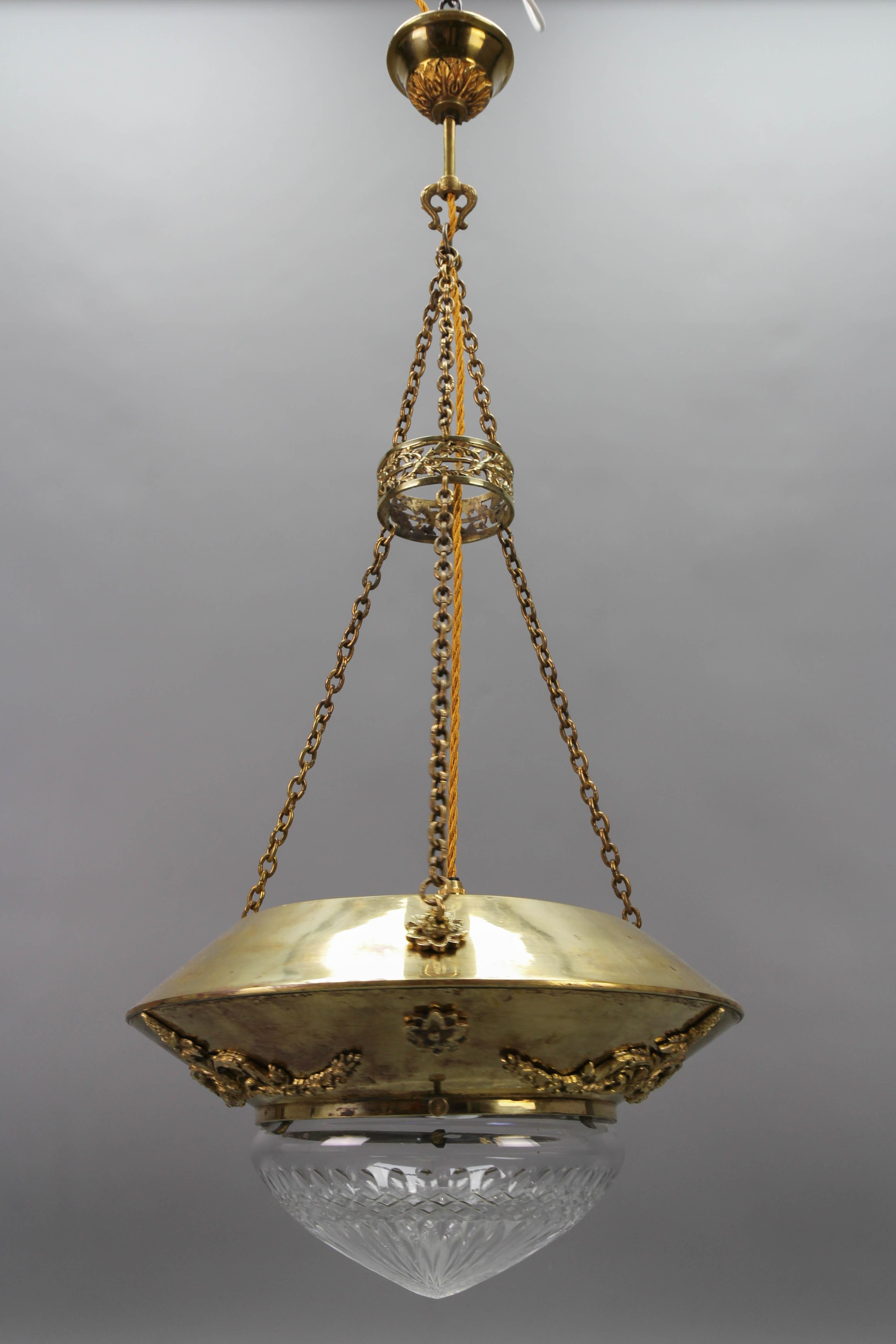 Antique French brass and bronze pendant light with cut glass lampshade from the circa 1900.
This beautiful antique neoclassical style pendant light features a brass body adorned with bronze decors and hung on three chains, a beautifully shaped