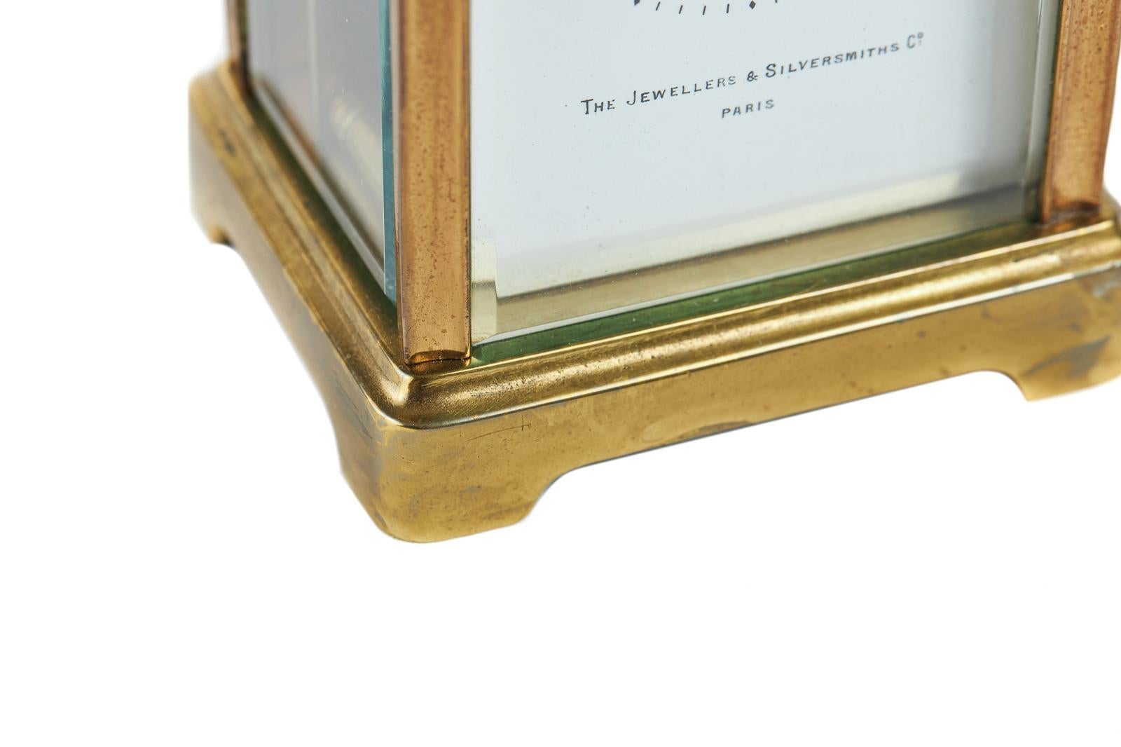 Antique French brass carriage clock which has a brass case with beveled edge glass and decorative handle with engraving of initials and date to the top, a white enamel dial with Roman numerals above The Jewellers & Silversmiths Company, Paris. It