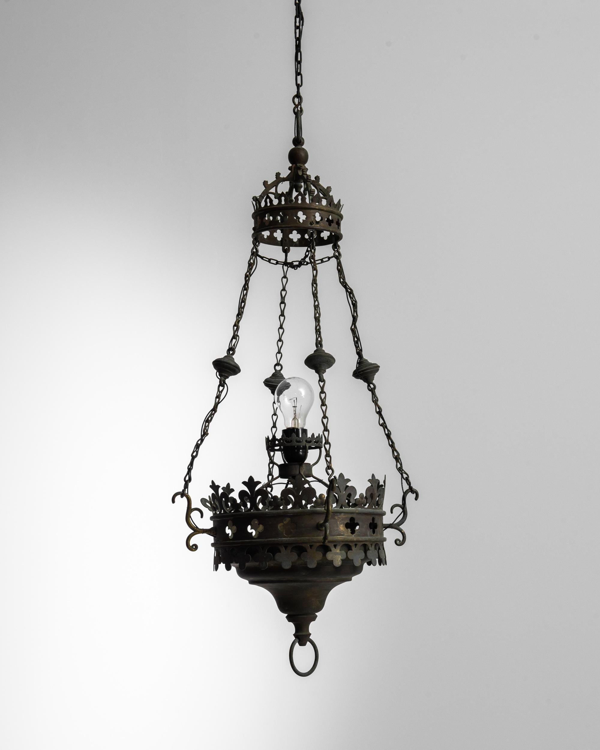This vintage metal chandelier lends a note of gothic glamor to your space. Made in France in the 1900s, a design of coiling brass scrolls and decorative ornaments— evocative details which gift this piece a darkly flamboyant personality. The crowning