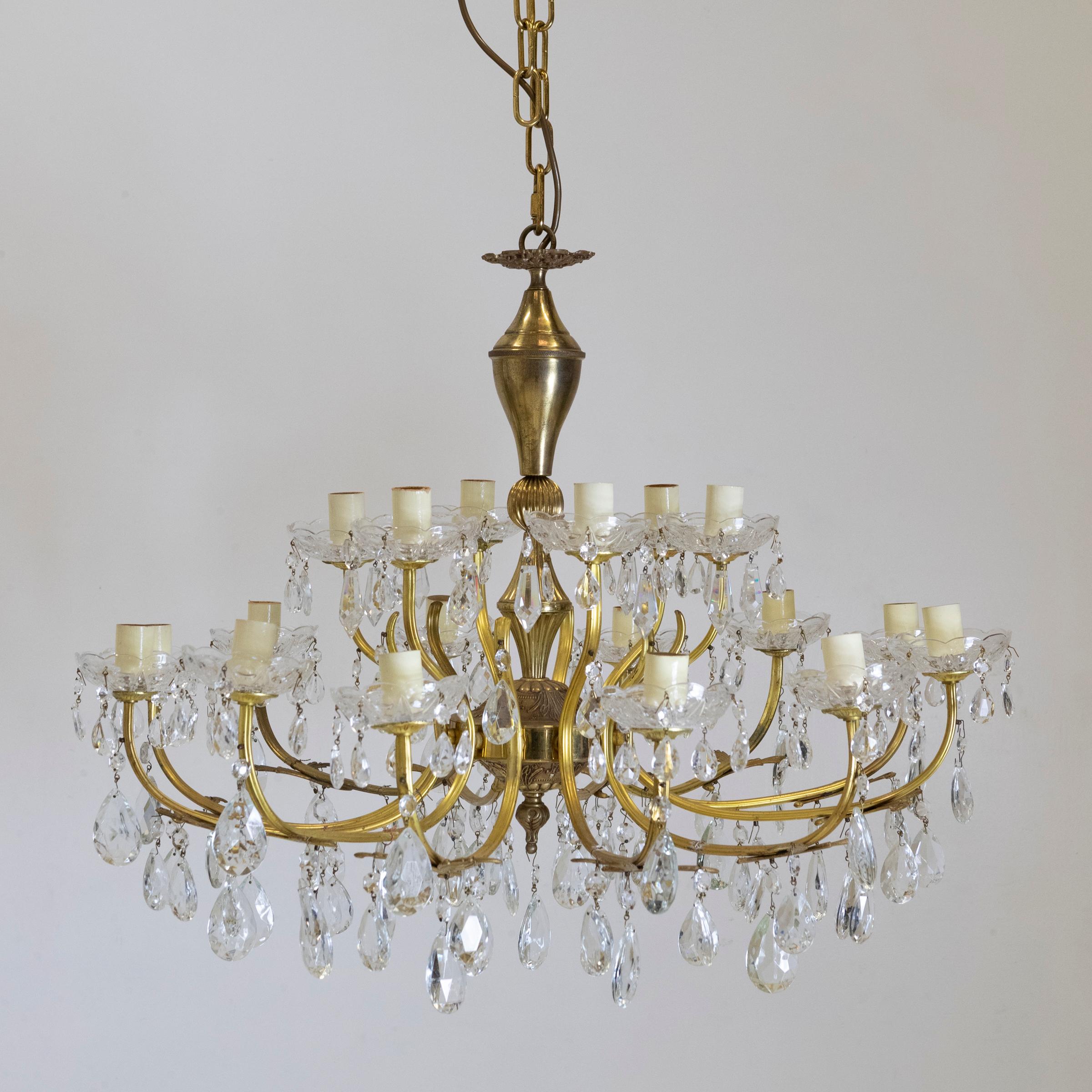 This antique French chandelier has 18 brass arms spread over 2 tiers. Each ornate arm terminates in crystal cut drip trays with multiple crystals suspended from each. A very pretty and substantial feature light.

Although in working order, due to