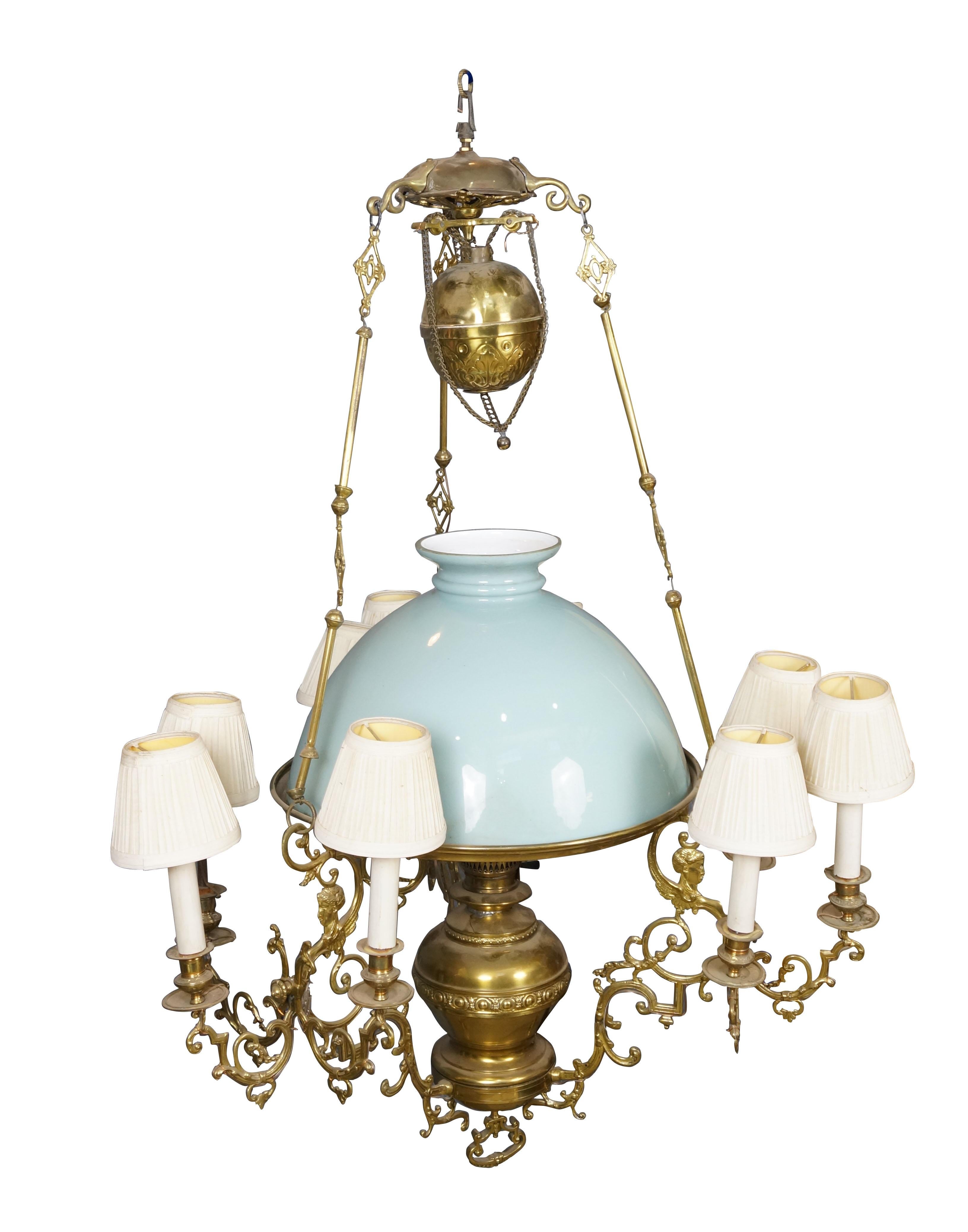 Lámpara / farol / araña de aceite y velas de nueve brazos convertida de finales del siglo XIX. De latón, con intrincados brazos de volutas tachonados de cabezas de esfinge. La bombilla central está sombreada con una pantalla de cristal celadón.