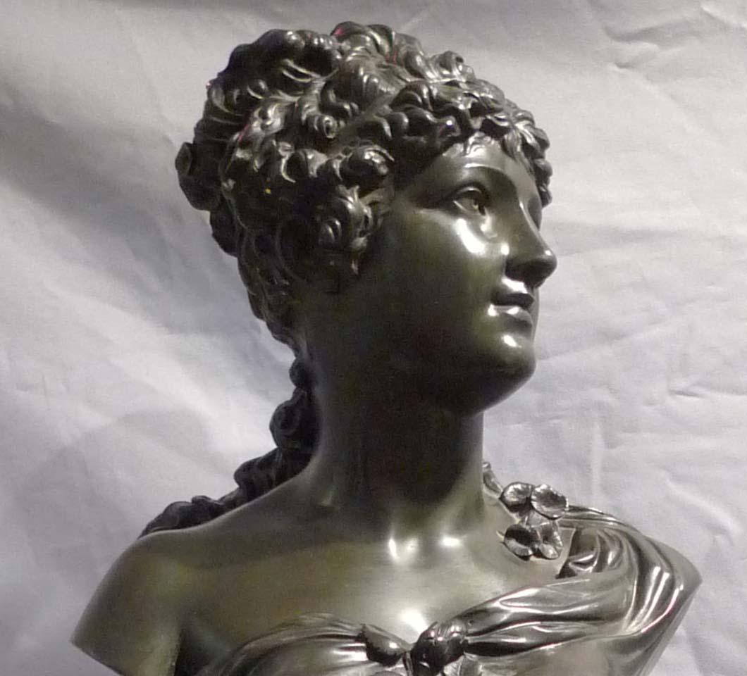 A very attractive antique bronze of a young woman, mounted on a marble base. The young girl with her hair up, one shoulder bare and with a rose in her bodice. She stands upon a reeded black marble column set upon a square base. A really fine object.