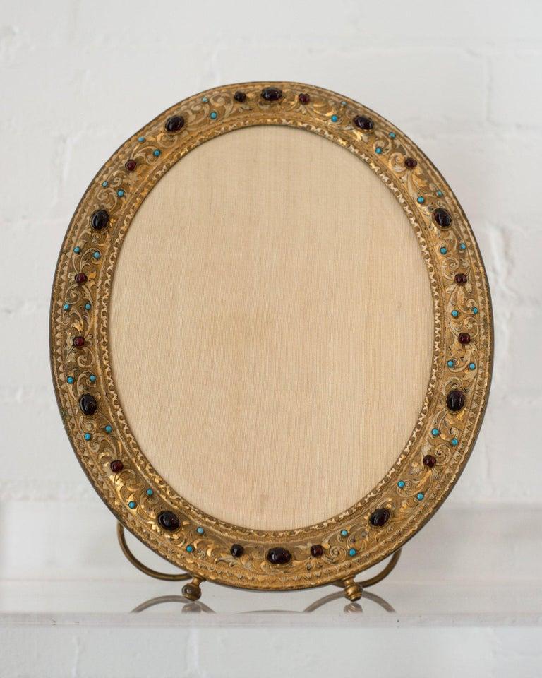 Un marco de bronce antiguo extremadamente decorativo con cabujones semipreciosos de color rojo y turquesa. Este marco es tan valioso como el recuerdo con el que lo llenes.