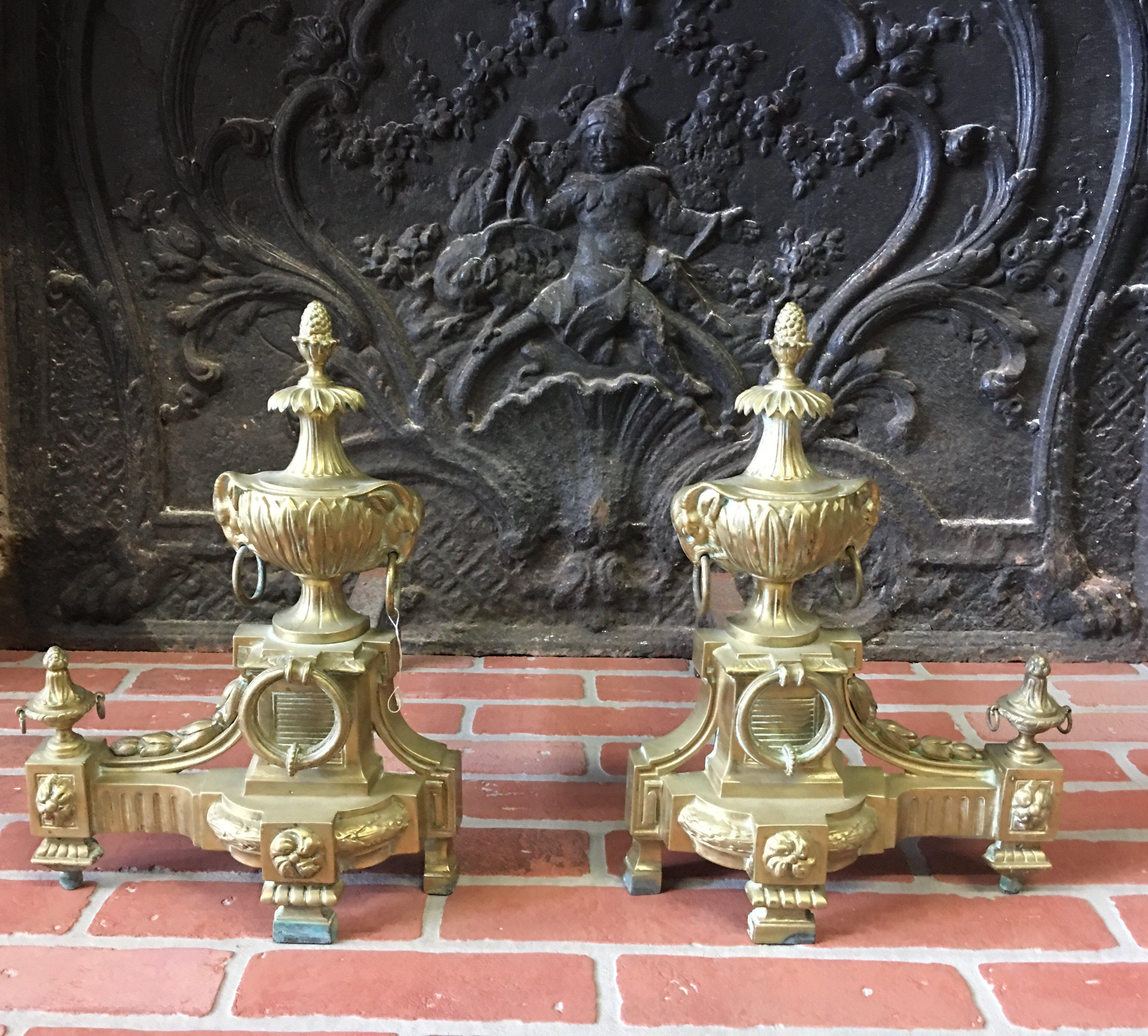 A pair of fine quality French bronze chenets in the Louis XVI style with small pineapple finials on stylised palm trees above bulbous leaf wrapped urns mounted on decorative ringed bases. French, mid-late 19th century. Measures: Width 11