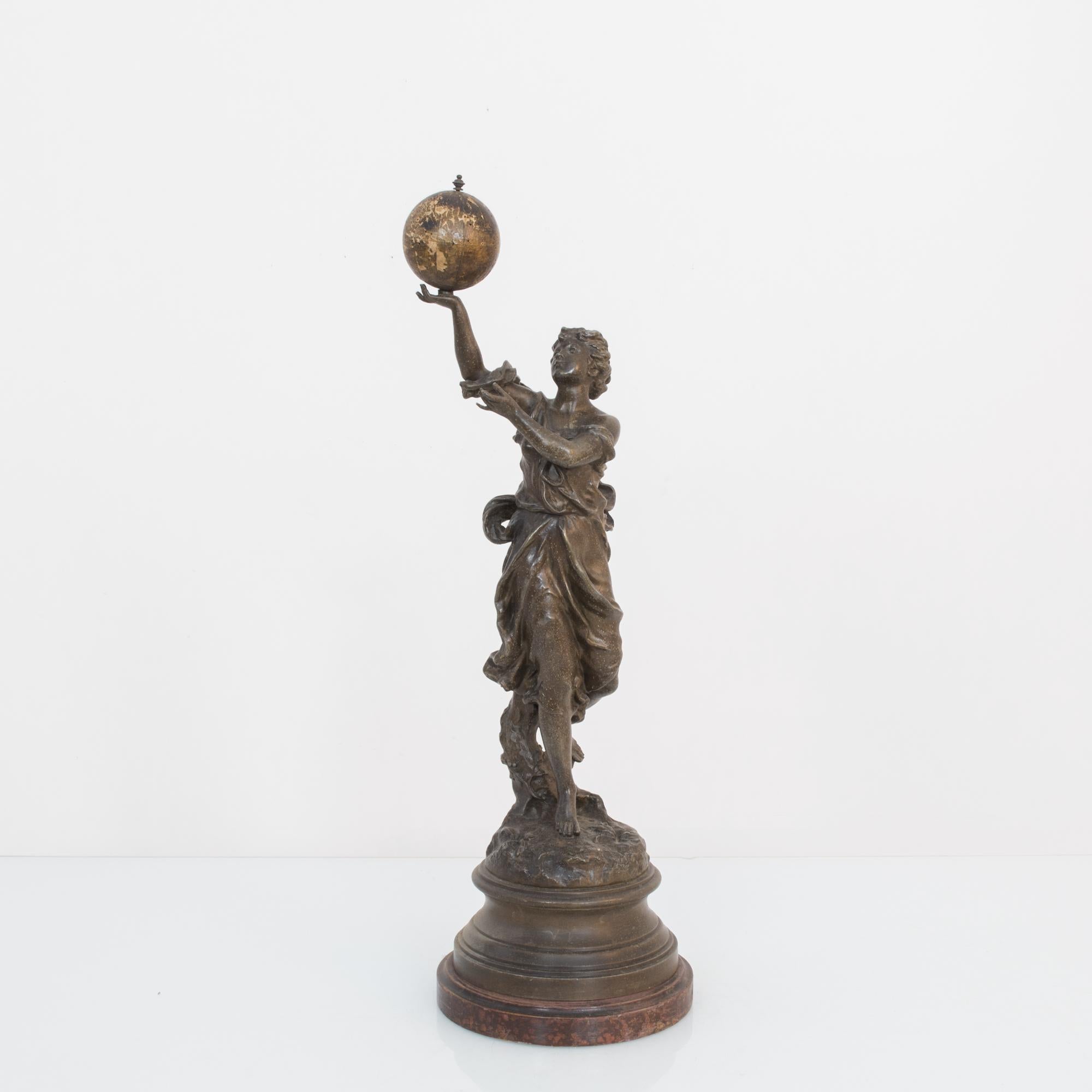 A bronze sculpture of a female figure created in France, circa 1900. This world toting muse is crafted in bronze with wooden accents, globe and socle. Her enchanted gaze gives us a moment of introspection on the world, our plans and travels, past