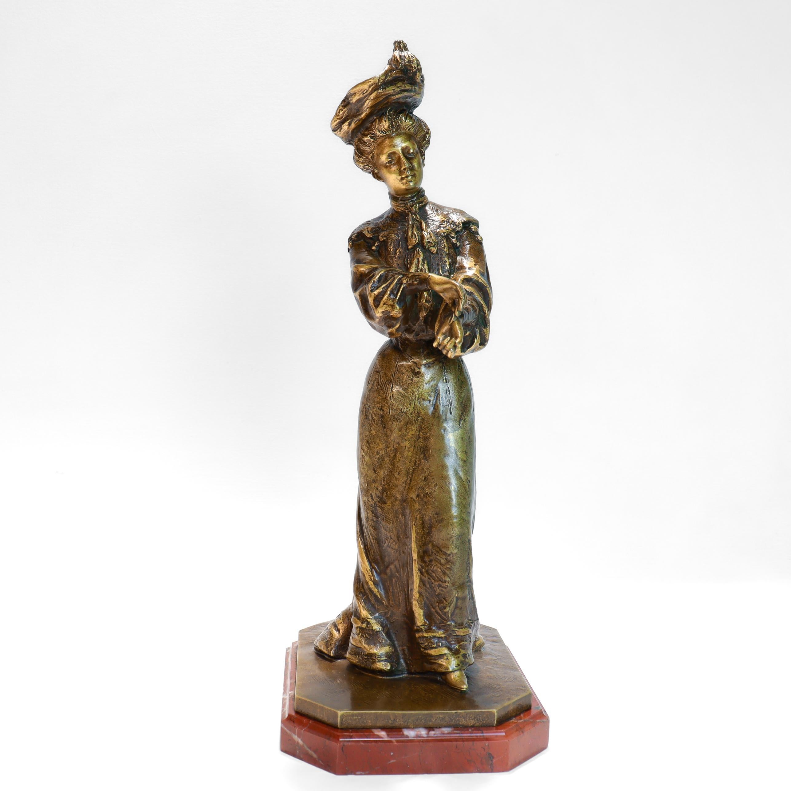 A fine antique French bronze sculpture.

By Louis Lerolle (ca. 1868-1948)

In gilt bronze with a darkened finish.

In the form of a well-dressed woman with a large hat putting on a glove.

Mounted on a red marble plinth.

Marked for L. Lerolle to