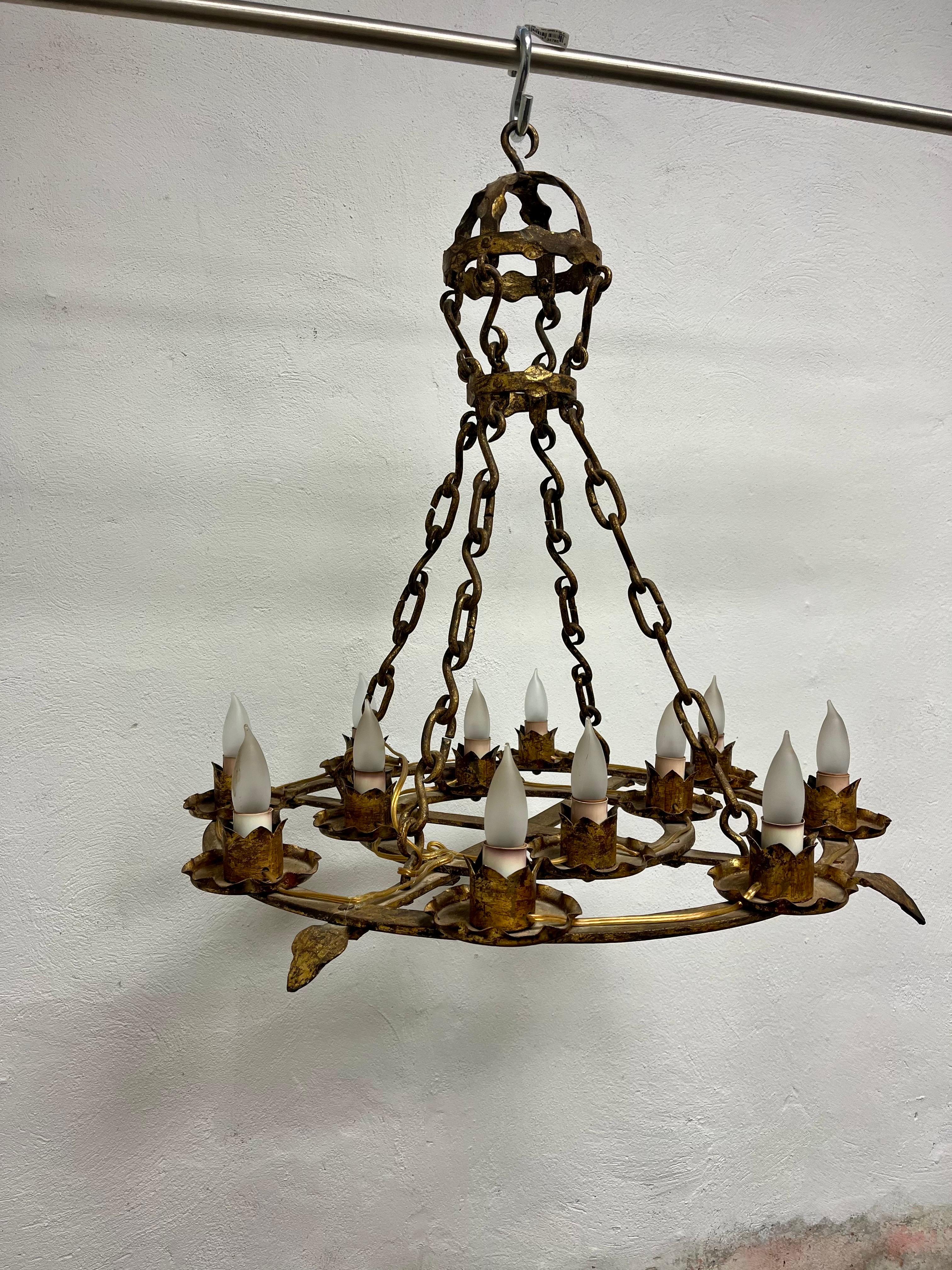 Large and heavy forged iron chandelier in brutalist, gothic, or medieval styling. Nice gilt finish. 12 candle with flame cups. Substantial presents with heavy chain leading up to crown like cap. 
Curbside to NYC/Philly $450