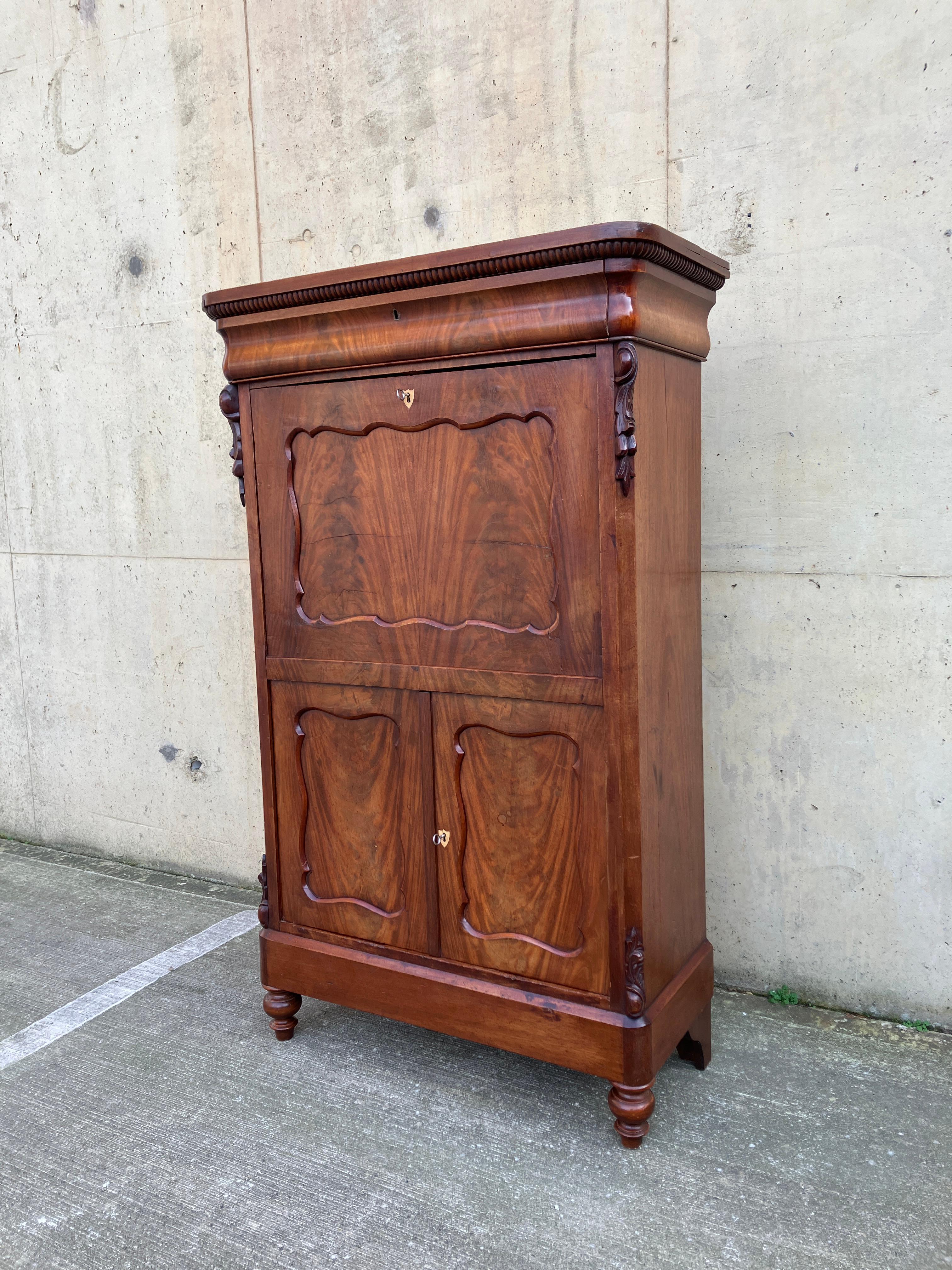 Precioso secretaire/bureau/gabinete de caoba flameada Antique French. El interior está forrado de arce y acabado con detalles en negro ebonizado. El armario tiene mucho encanto y carácter, con impresionantes decoraciones talladas. La caoba flameada