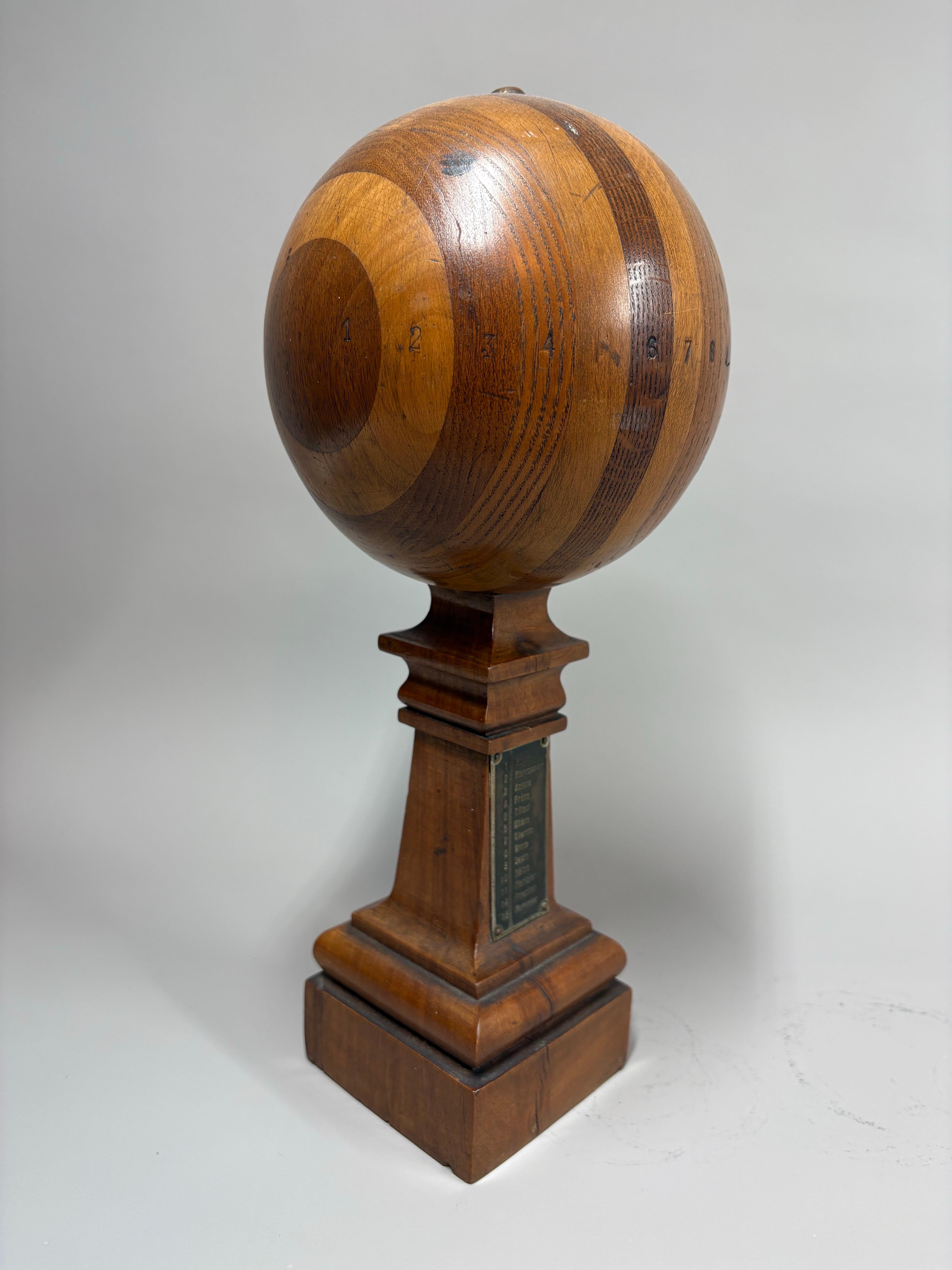 Un échantillonneur en bois d'ébéniste français ancien, finement travaillé, présenté sous la forme d'une sphère montée sur un piédestal carré. La base comporte une plaque métallique personnalisée identifiant chaque essence de bois utilisée dans la
