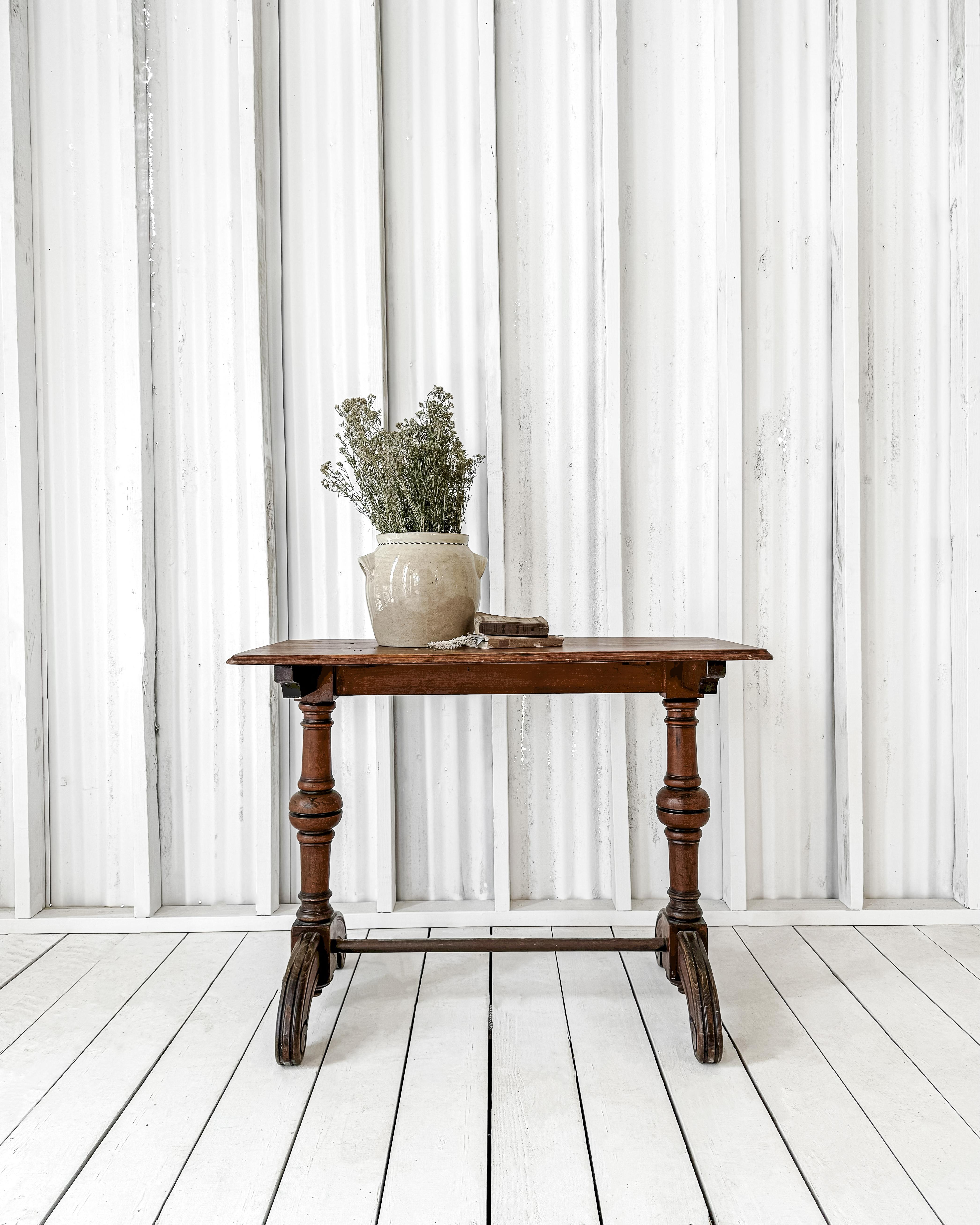 A charming café table perfect in size for use as an accent table or small console. The rectangular molded edge top rests atop a metal trestle base with wide, elegantly contoured carved feet. Diamond-point stretcher blocks and the graceful shape of