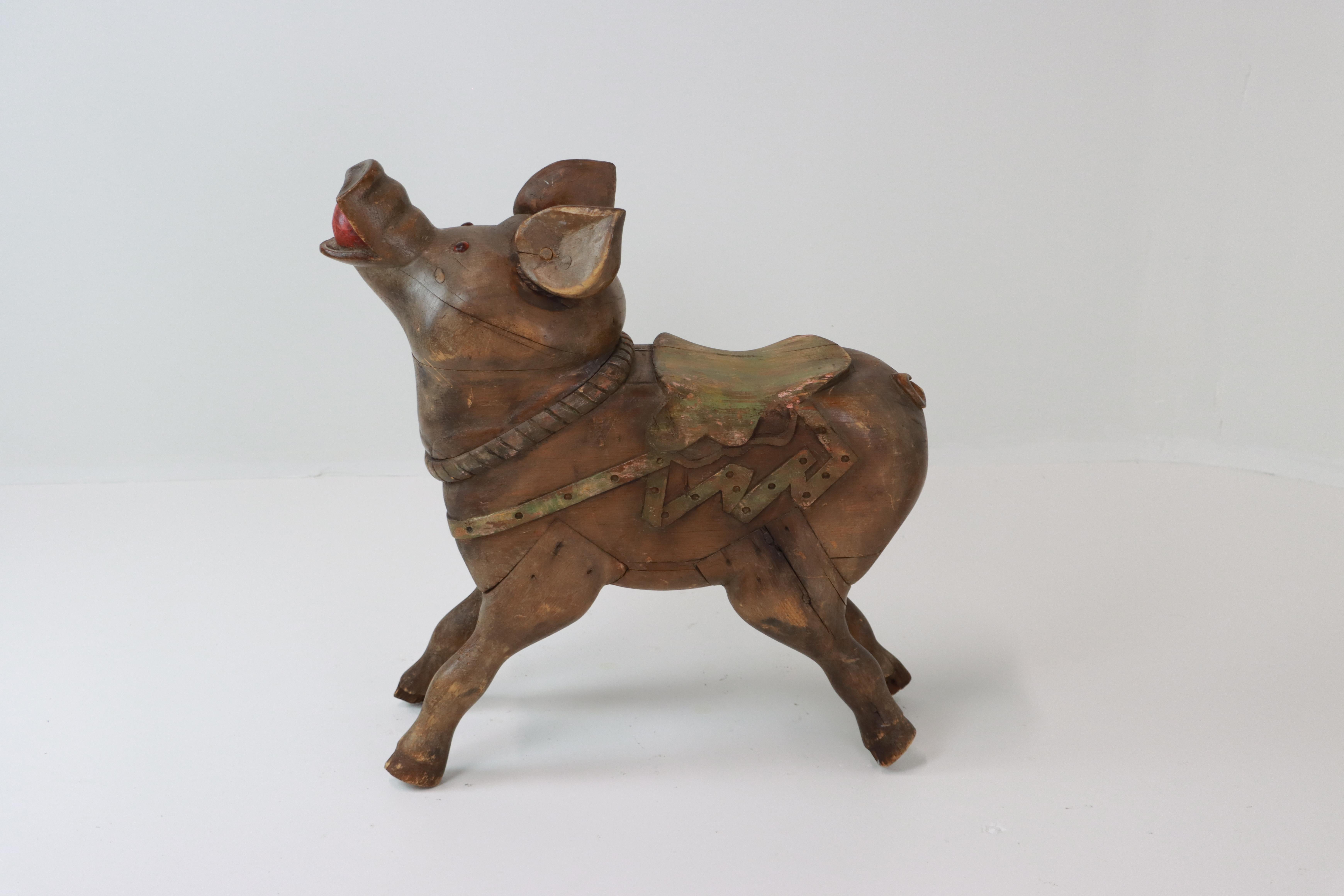 A rare and whimsical example of a French fairground carved wooden pig it was most likely from the traveling manèges forains (carousel rides). His happy, upturned head shows a red apple in his mouth, inset glass eyes, and a carved saddle accented