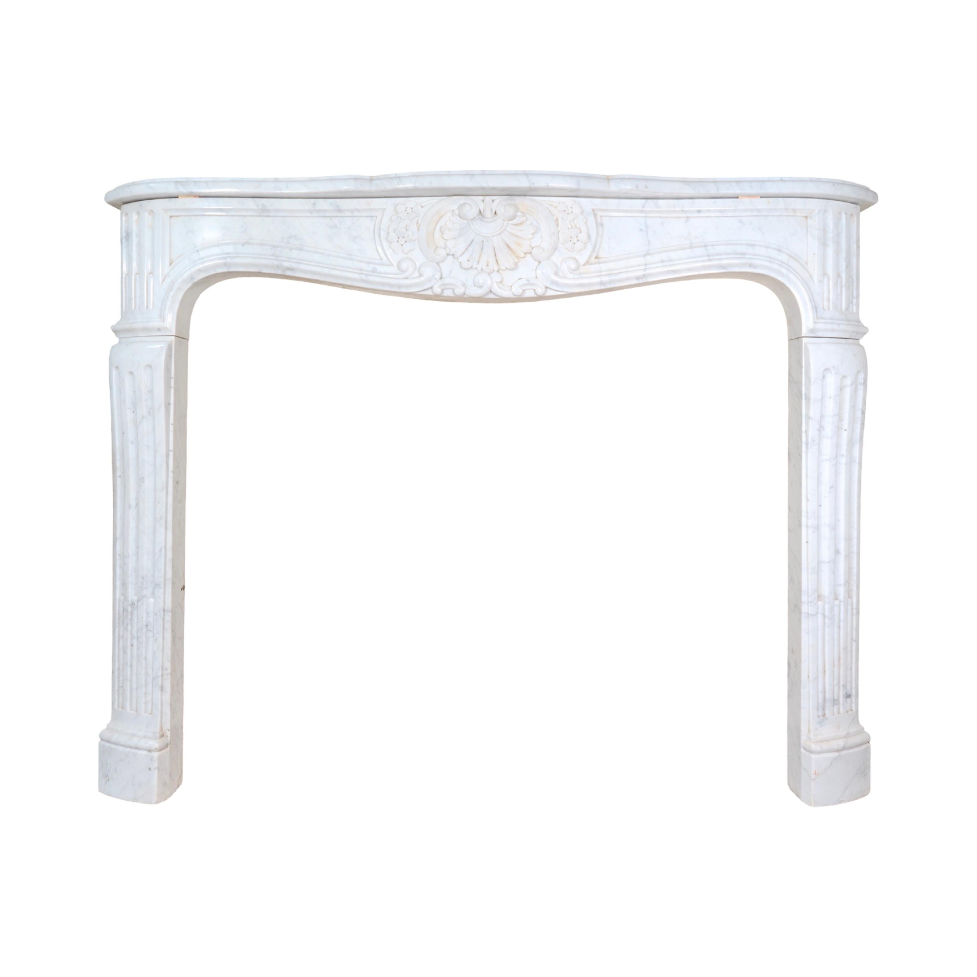 An elegant 19th-century French mantel carved from Carrara marble, showcasing the refined curves and ornamentation of the Louis XV style. The serpentine front is centered with a carved shell cartouche, flanked by scrolling foliage and floral motifs,