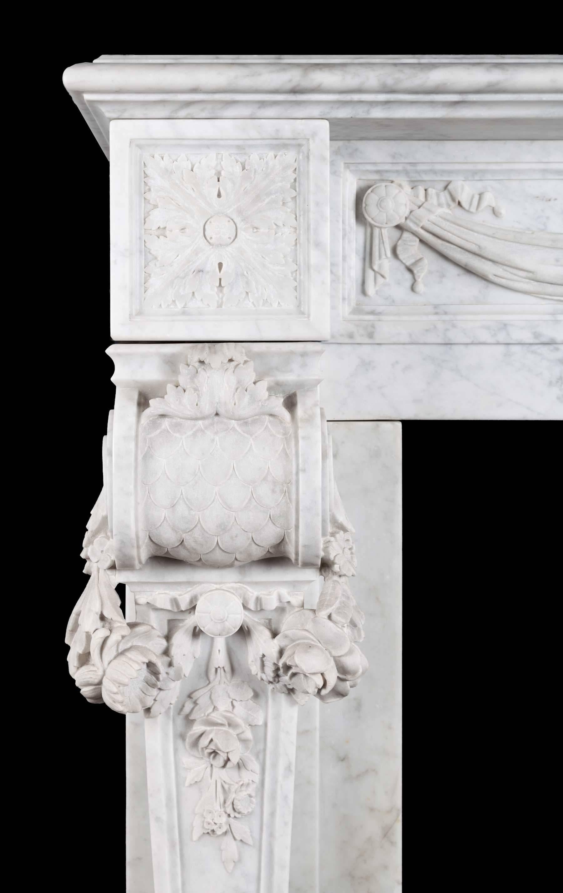 An antique French Carrara marble mantelpiece in the Louis XVI style. The swags of drapes frieze, centered by a plaque that is carved with a classical urn and arabesques. The square foliate paterae corner blocks rest on console jambs, which are