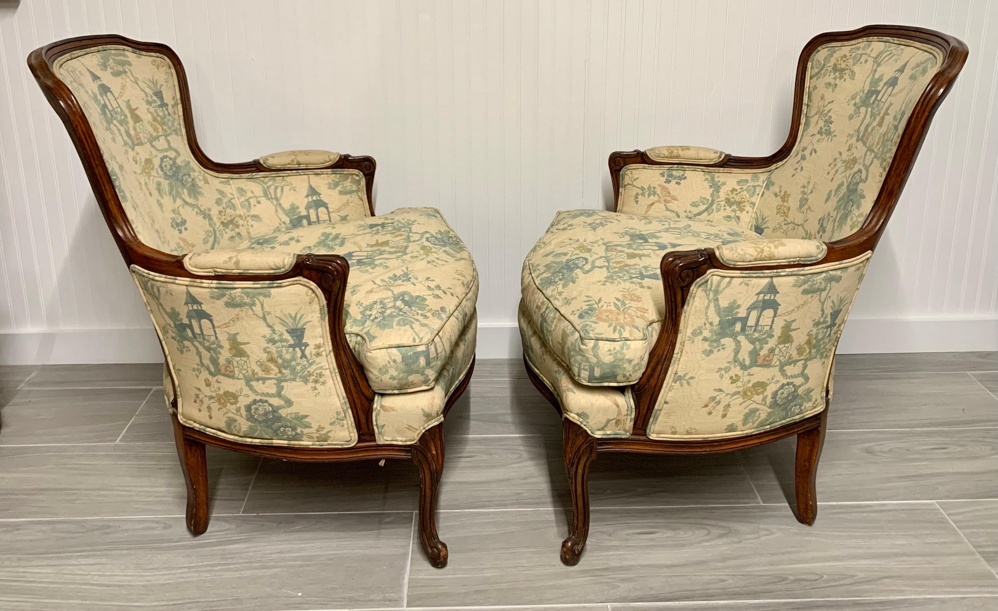 Elegant French bergeres with carved walnut frames and chionoiserie style upholstery. Loose down seat cushion.