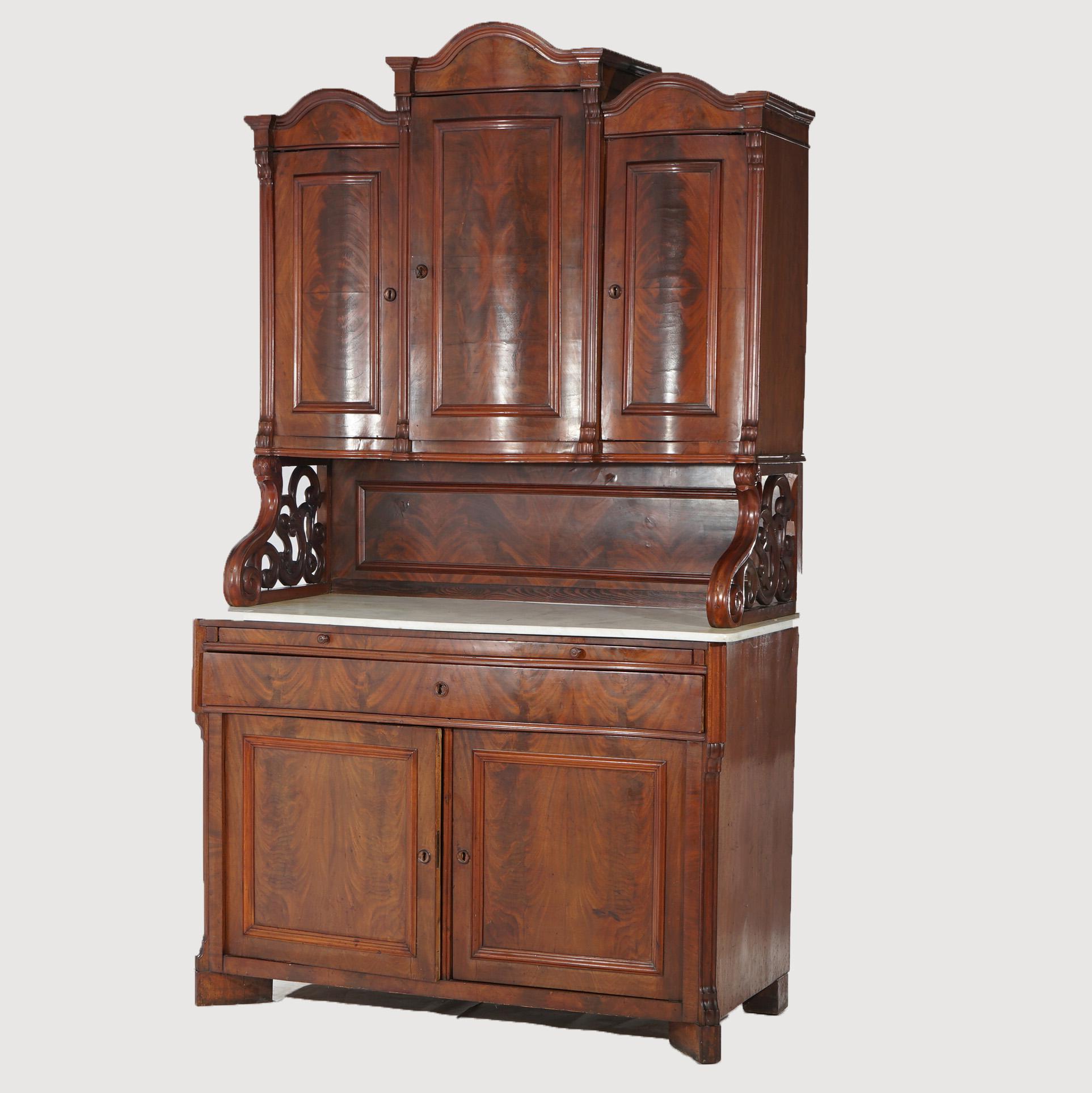 An antique sideboard offers flame mahogany construction with upper case having arched pediment over triple blind door cabinets, raised on foliate carved supports surmounting lower marble top case having slide-out server, single long drawer and