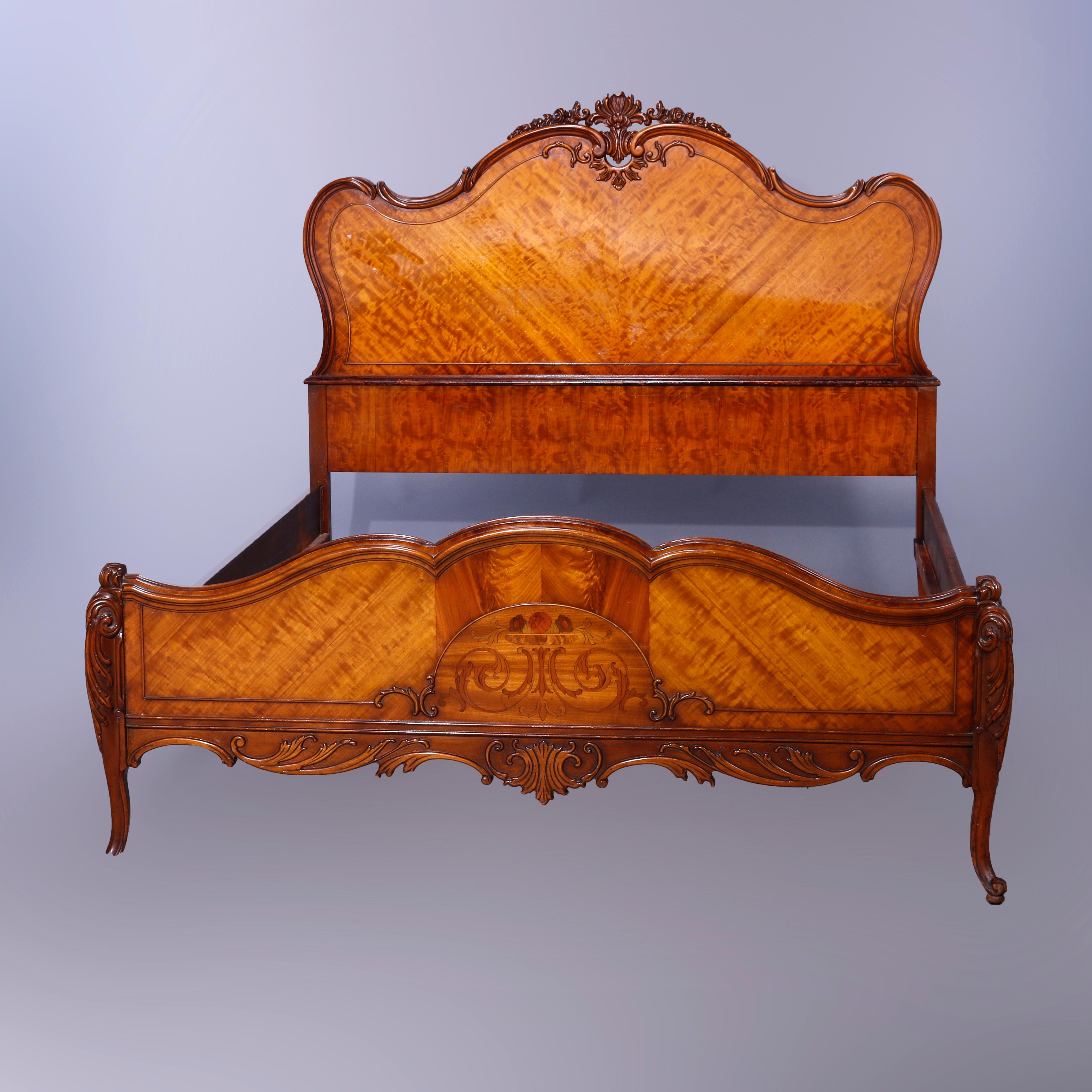 An antique French double bed offers mahogany frame with carved foliate crest over shaped headboard having bookmatched satinwood facing, matching footboard having marquetry inlaid urn and scrolled foliate design, raised on cabriole legs having carved