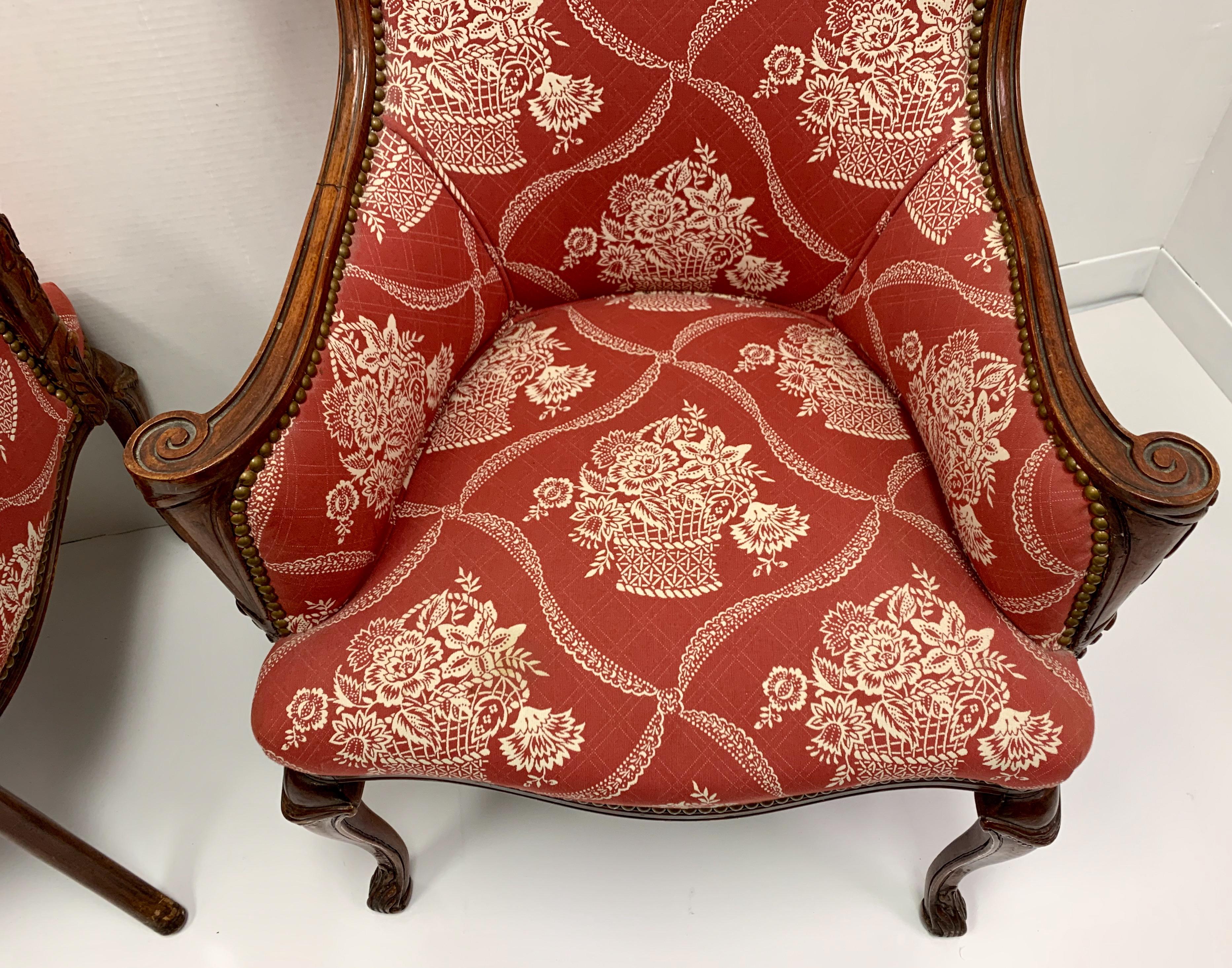 This is a pair of antique French carved mahogany wing chairs in a vintage Schumacher red and white fabric. They have brass trimmed nailheads and carved scrolled arms. They are unmarked and in very good condition. Arm; 24”.