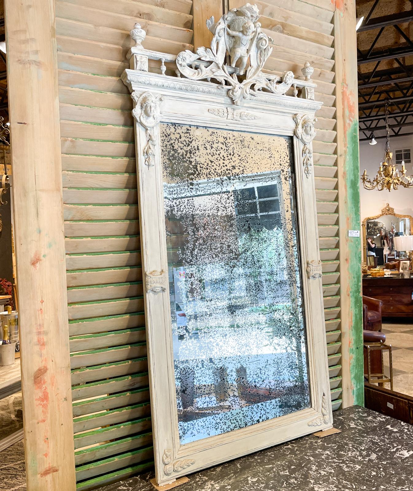 This antique French mirror features a beautifully carved frame and beveled glass with distressed mirror. The frame has ornate floral carvings and details along the sides and bottom edge and a very ornately decorated top edge, including a detailed