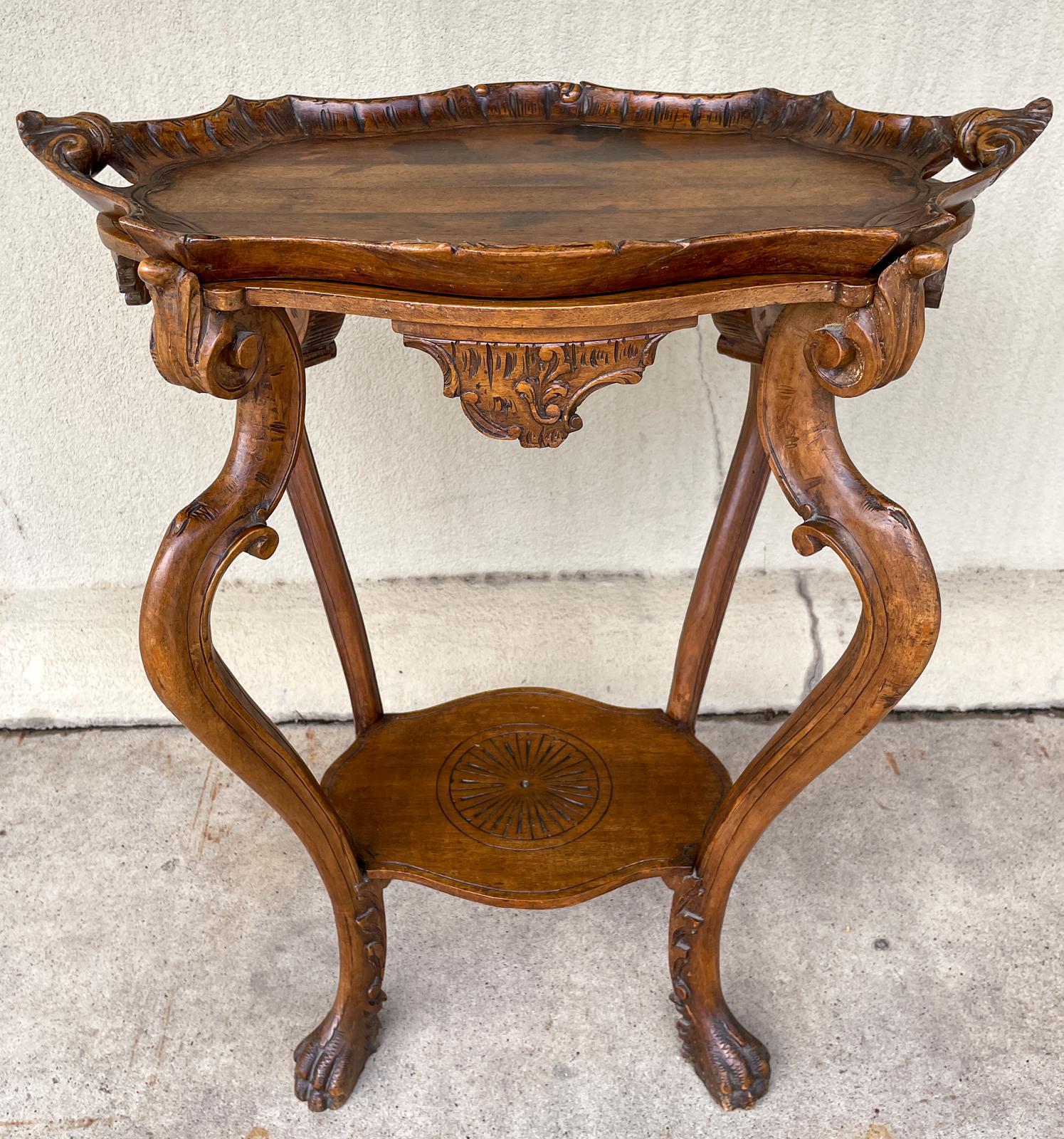 This antique French tray-top side table is crafted in oak and features a number of decorative details, including beautifully curved legs ending in paw feet, a sun medallion on the lower shelf and carved decorative accents on the apron. The top is