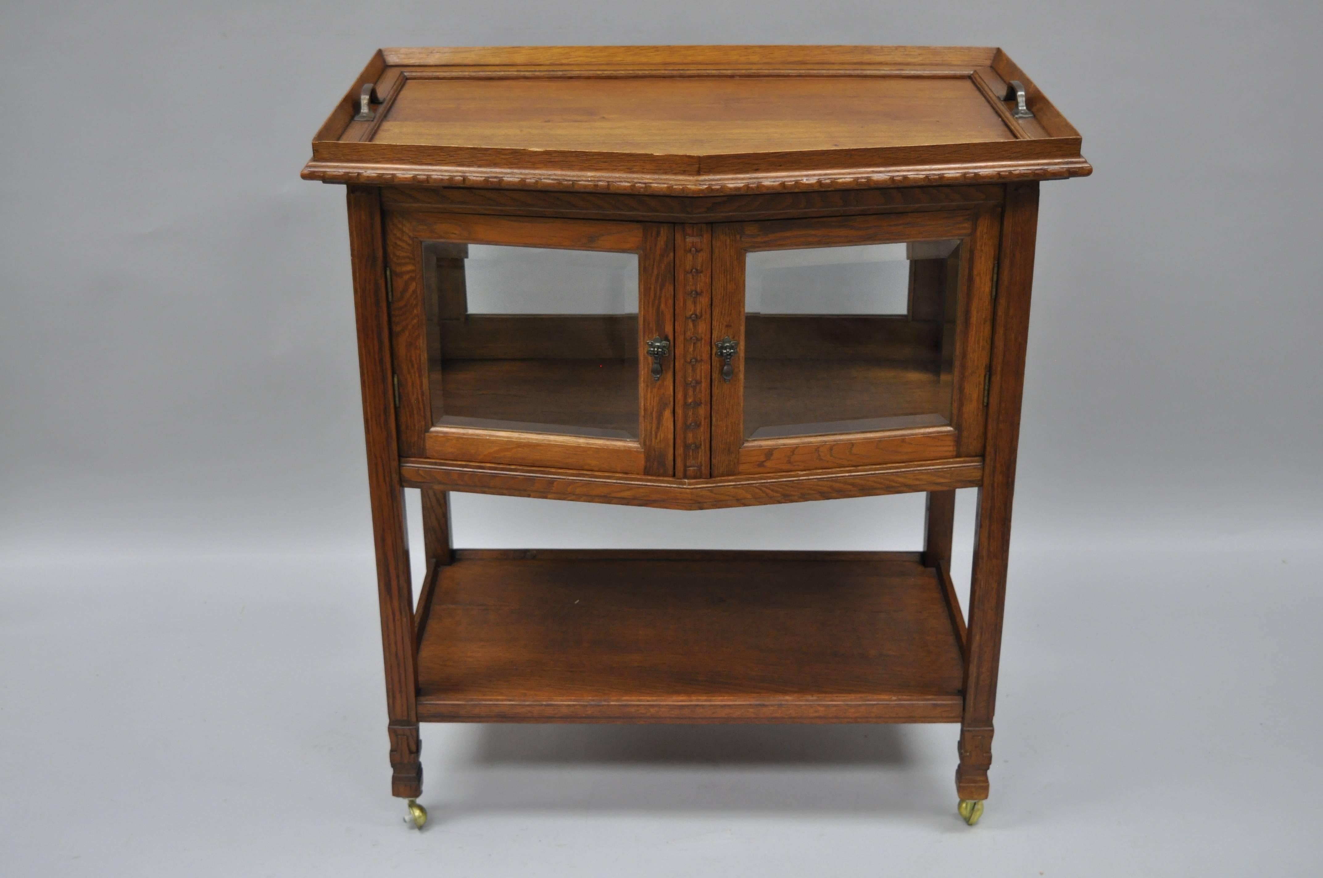 Antique French carved oakwood server bar cart or display cabinet. Item features a removable serving tray top, bevelled glass front and side panels, rear panel glass, rolling casters, lower shelf, beautiful wood grain, and nicely carved details.
