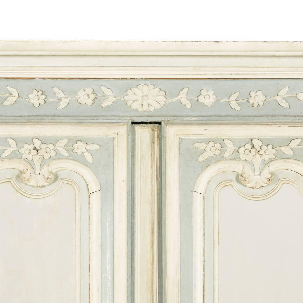 A 19th century French two-door armoire with floral carved details throughout, elegant shaped panelled doors, and scrolled feet.
Soft blue/grey chalk paint in three tones highlights the panels and carving.
An elegant and practical French piece