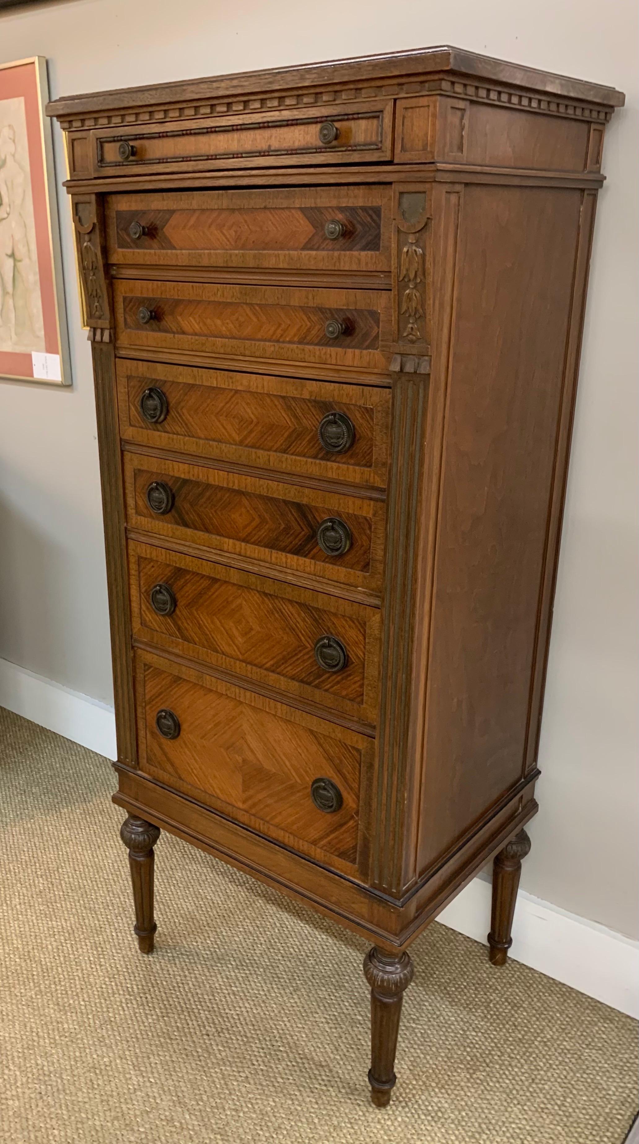 Antique carved mahogany lingerie chest has seven dovetailed drawers and features parquetry on drawer fronts and carved detail all around. It is raised on four carved fluted legs. Original brass hardware.