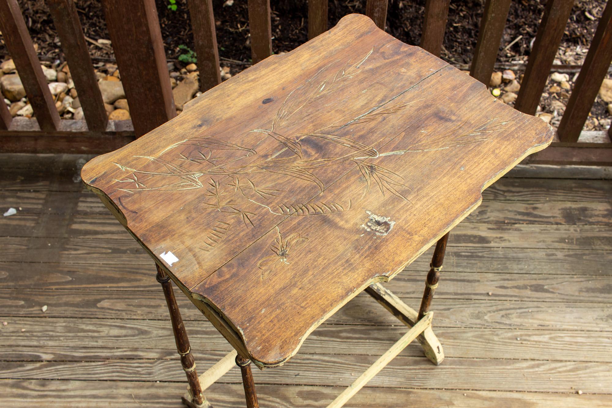 This delicate side table features turned legs and a wonderful carved top with a decorative edge. The image in the top shows some foliage and a dragonfly figure. The paint remaining on the piece is pale yellow and there appears to be some patinated