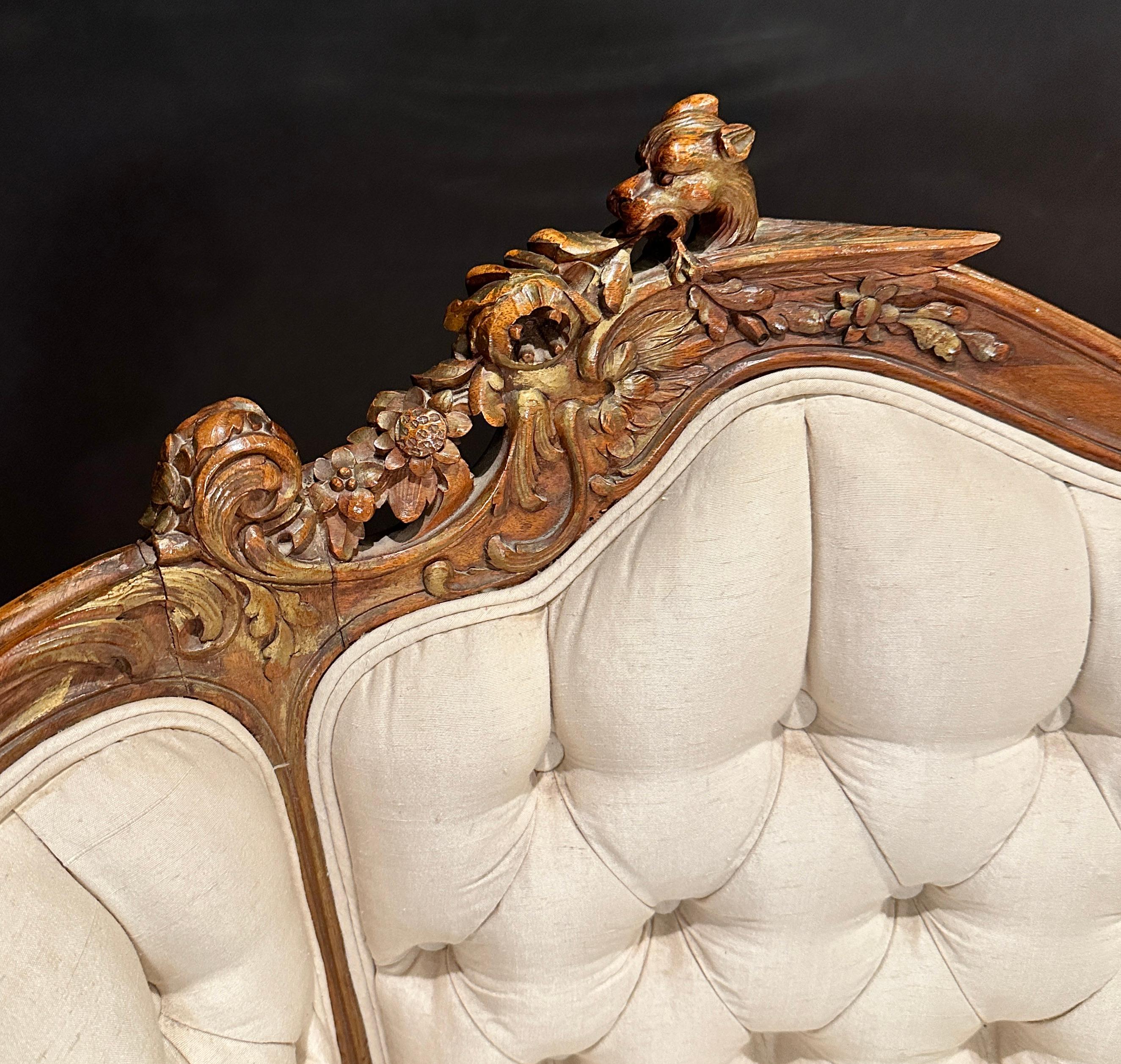 Antique French 19th century carved walnut Bergère armchair. Features a detail carving of a winged lion or griffin at the crest of the left side. Scrolls and floral carvings throughout, all with faint highlights of gilding. Upholstered in an ivory