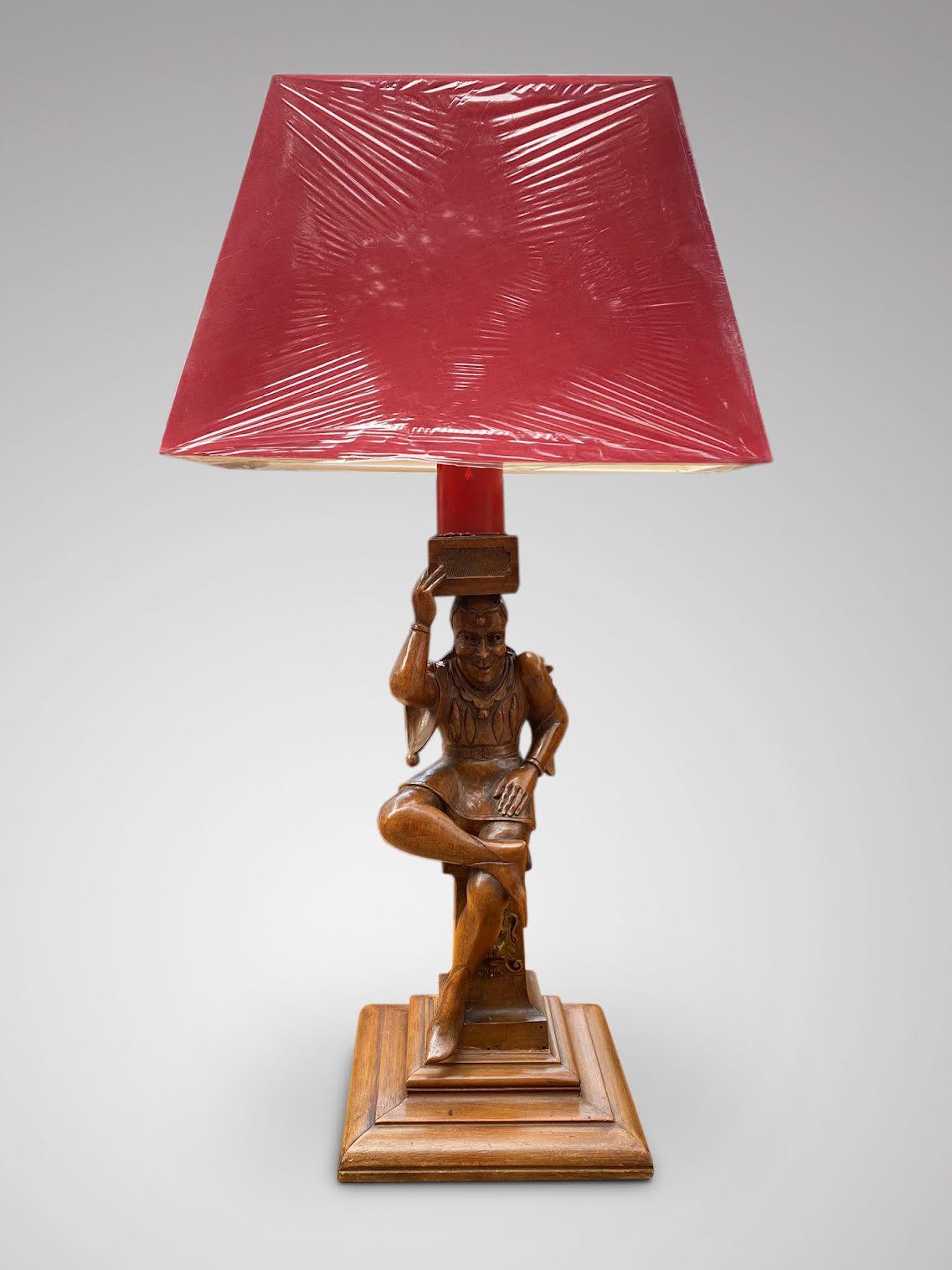 A 19th century French hand carved walnut sitting Court Jester mounted as a table lamp. Standing on square base, below a rectangular red lamp shade. The sculpture in very good condition and with a very warm patina. In working order.

The measurements