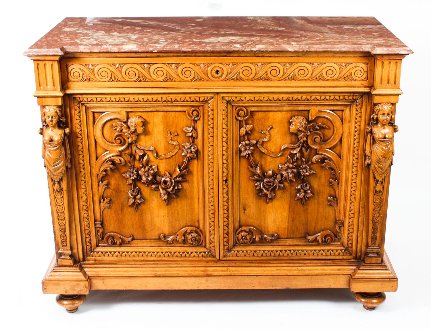 A 19th century continental walnut side cabinet, the rectangular mottled red marble top with a moulded edge above a long frieze drawer carved with vitruvian scrolls, over a pair of panelled cupboard doors decorated in relief with putti, floral swags
