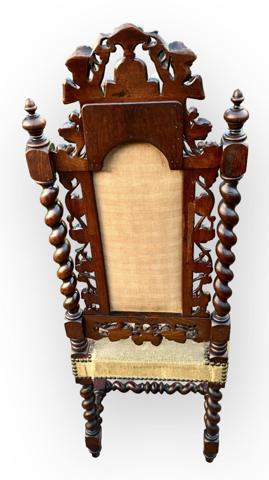 A fine French Victorian hand carved walnut high back chair with lovely ecclesiastical detailing on barley twist legs and united by a classic turned H-stretcher. 
Winged putto flanking a center scrolling crest and profuse grape leaf carving to the