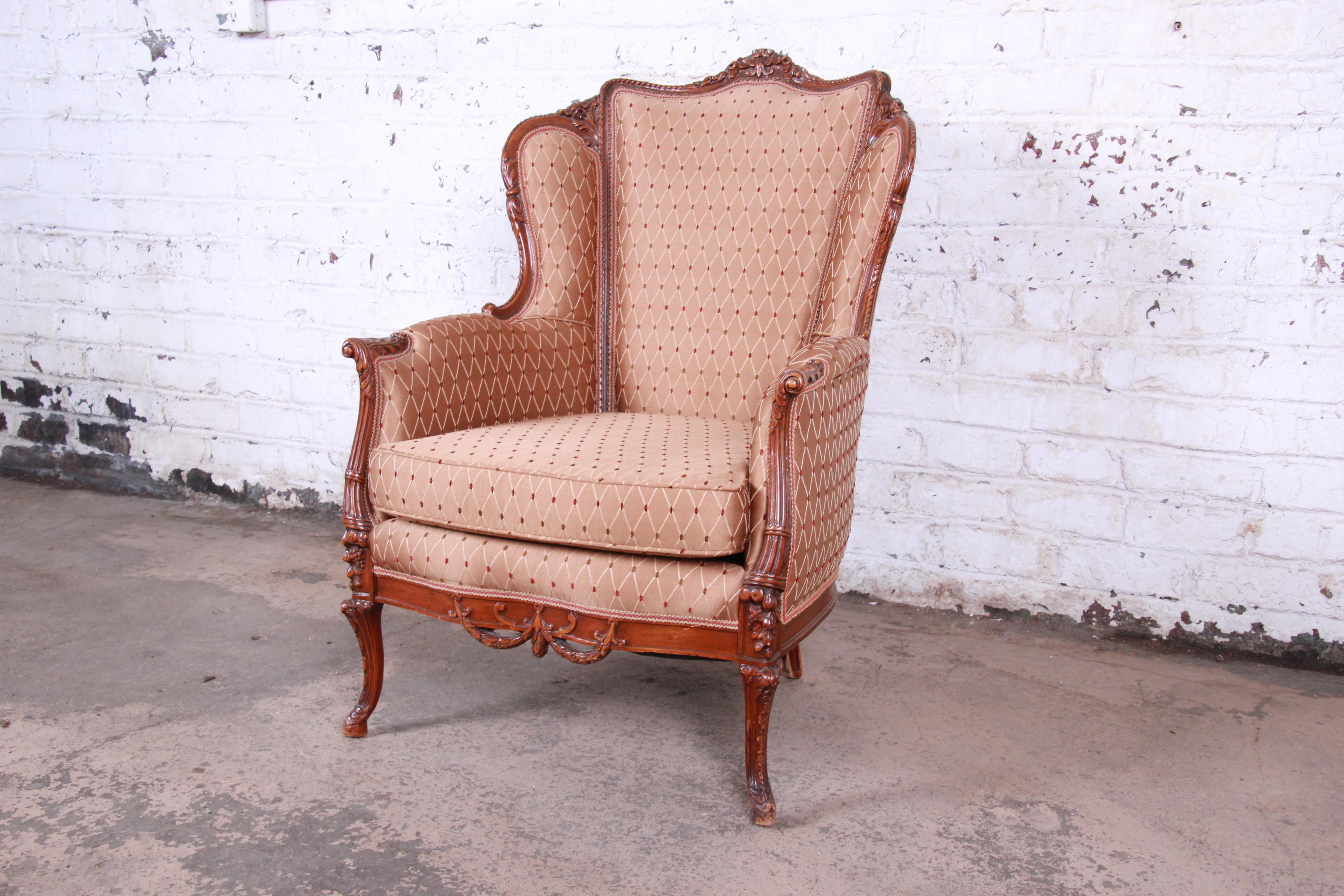 A gorgeous antique French carved wingback lounge chair, circa 1930s. The chair features a solid walnut frame with beautiful carved wood details. It has clean light brown upholstery with a diamond pattern in ivory with red accents. A very stylish and