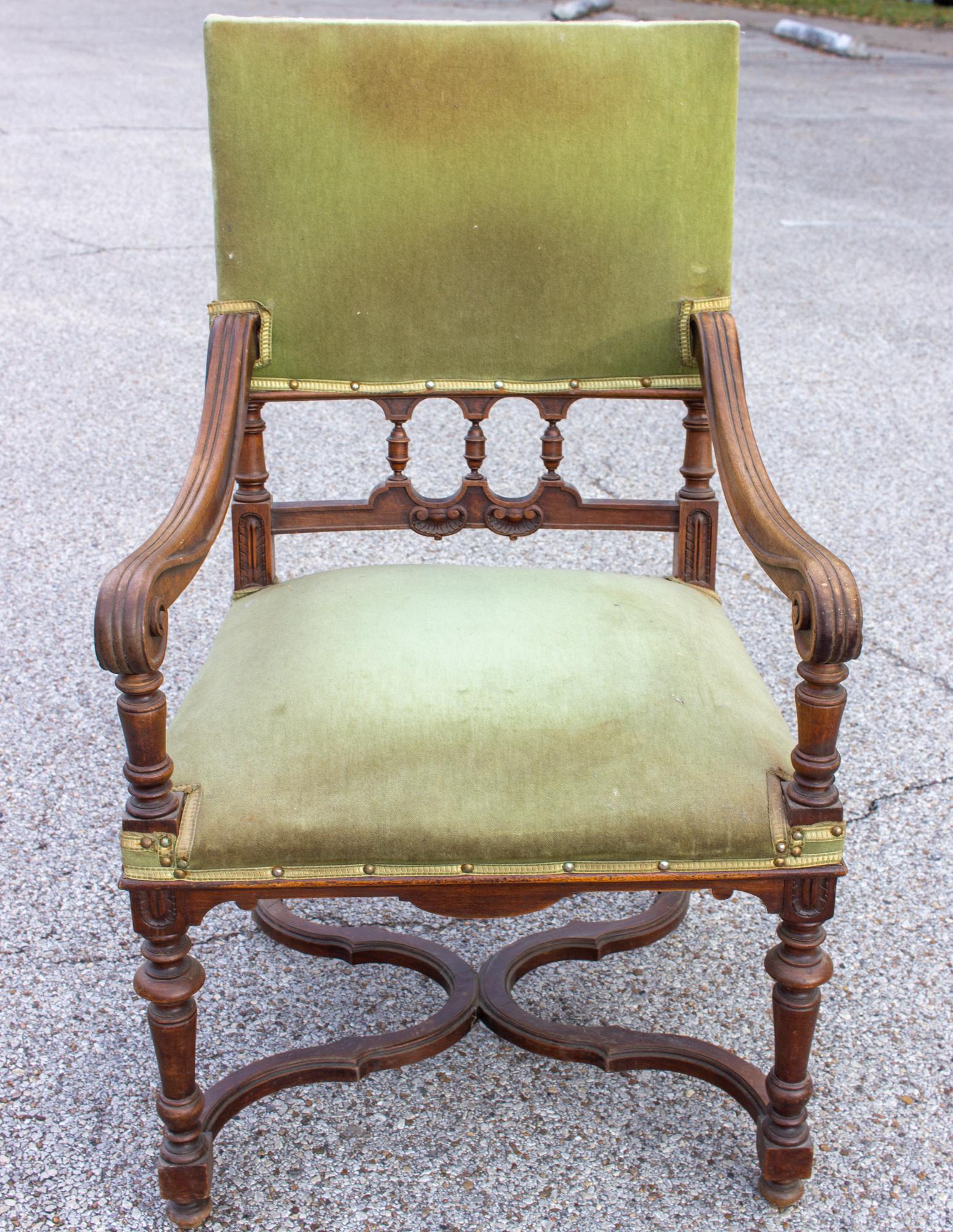 This generously sized antique French carved wood armchair features faded green velvet upholstery and various turned details the arms, legs and back. The arms gently curve down and forward, ending in a scrolled detail. The x-style base is beautifully