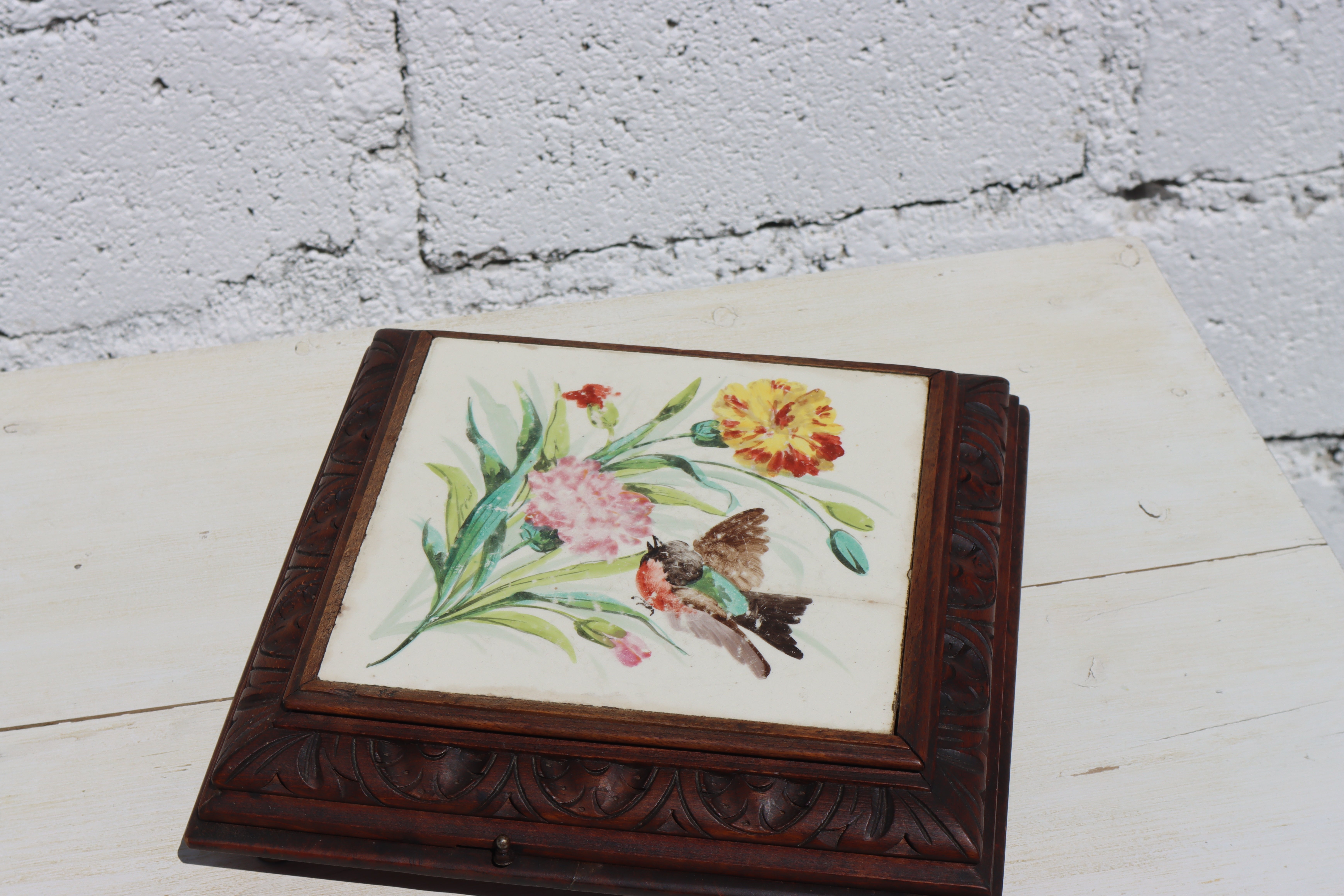 Wonderful vintage Table Decoration - hand-carved Walnut Music Box Trivet with Art Nouveau Motifs.
Colorful hand-painted Ceramic Art Pottery  Surface with Flower and Bird motif.

According to the label on the back, this box plays the Waltz