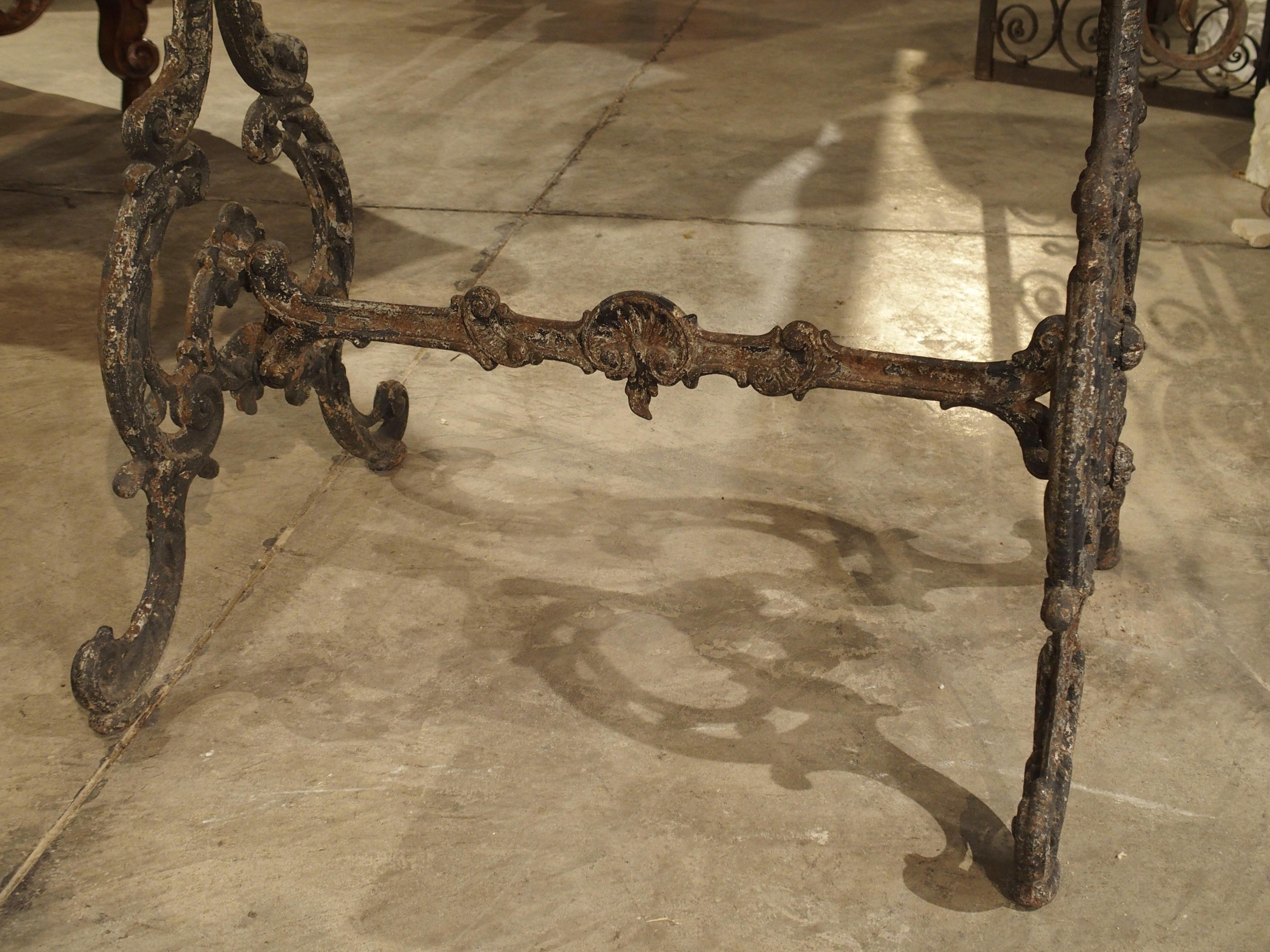 This beautifully designed antique iron garden table with marble top has thickly cast, but intricate designs to its ironwork. There are several variations of acanthus leaf C and S scrolls, along with shells making up the base of the table. It is not