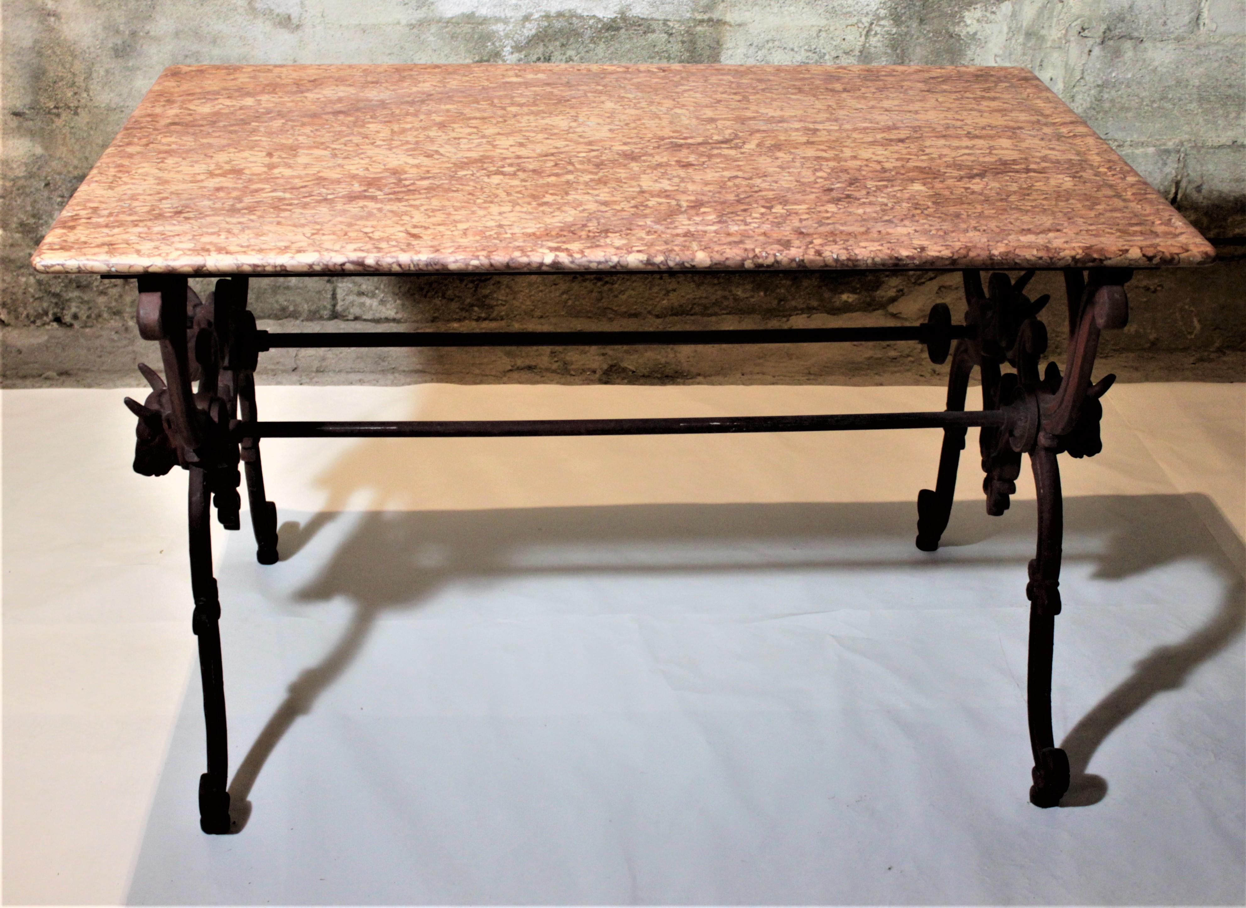 This antique French cast iron butcher's or conservatory marble-topped table was made in the late 19th century in the Victorian style. The base is very ornately cast with scrolled decoration and two figural cow heads on each of the trestle side