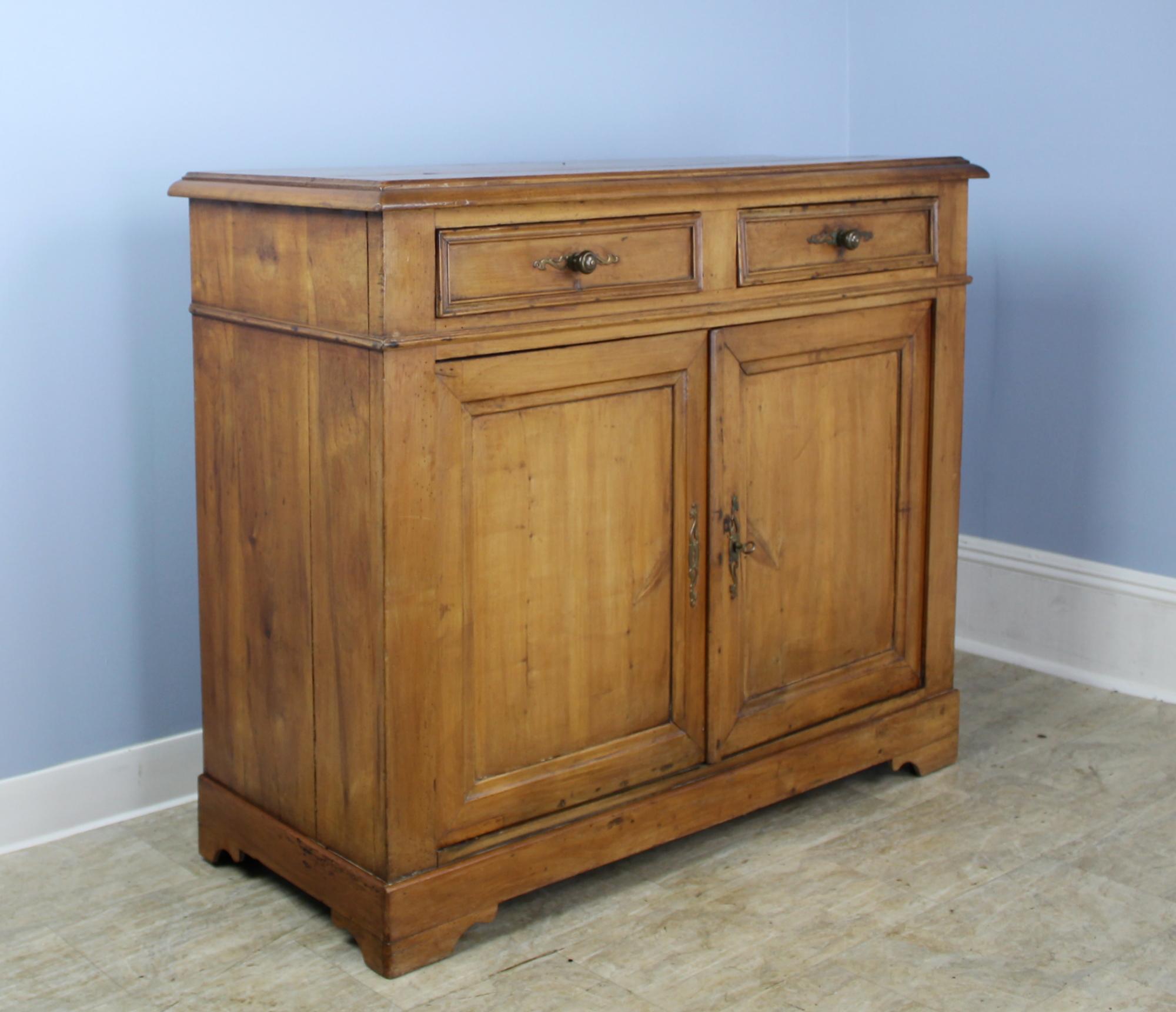 This is a wonderful example of the later Louis Philippe look, with shaped drawers, set-in panels on the doors, and handsome simple molding at the bottom. The lighter, warm cheerywood color is rich in patina, with some light distress on the top. Good