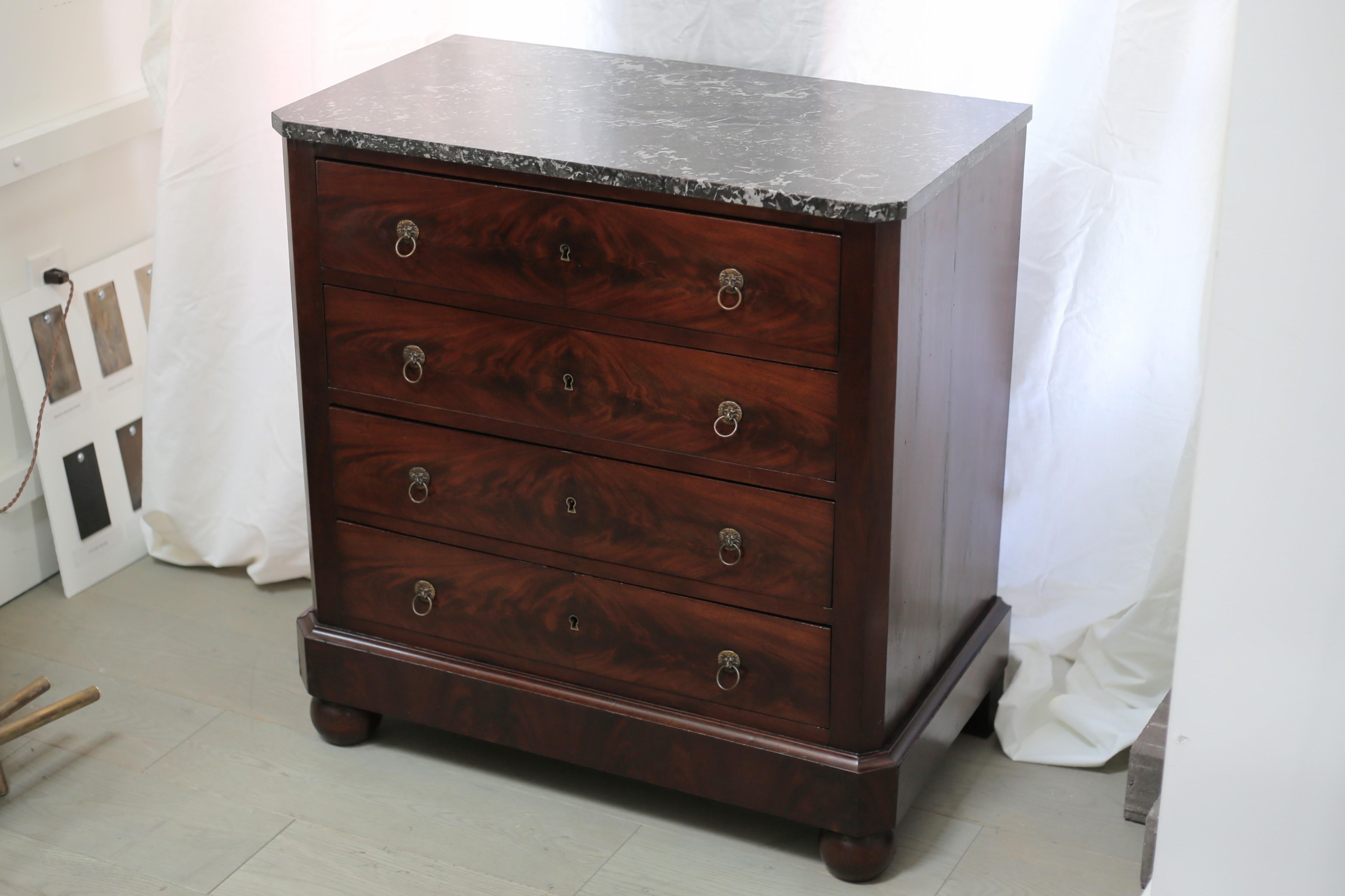A beautiful antique French four drawer commode/chest of drawers with chamfered corners, marble top, bun feet, and brass lion ring pulls and escutcheons. Dovetail drawer joinery and bookmatched flame mahogany veneer on the drawer fronts. The marble