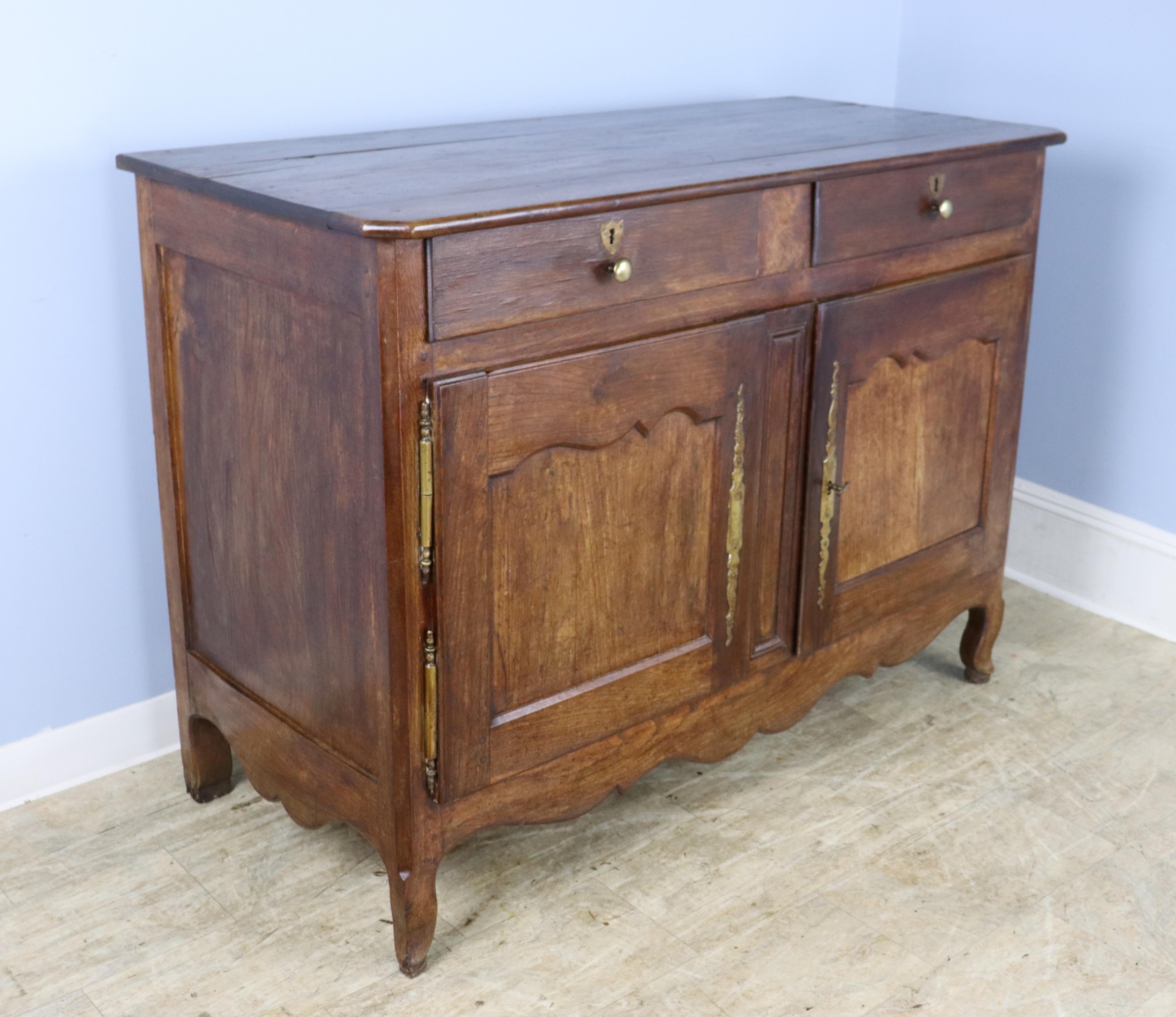 An antique country buffet with a scalloped apron from France. The chestnut has exceptional graining with a rich patina. See the beautiful chestnut wood used even on the top and doors. Lovely escutcheons and hinges. Two wide drawers above a cabinet