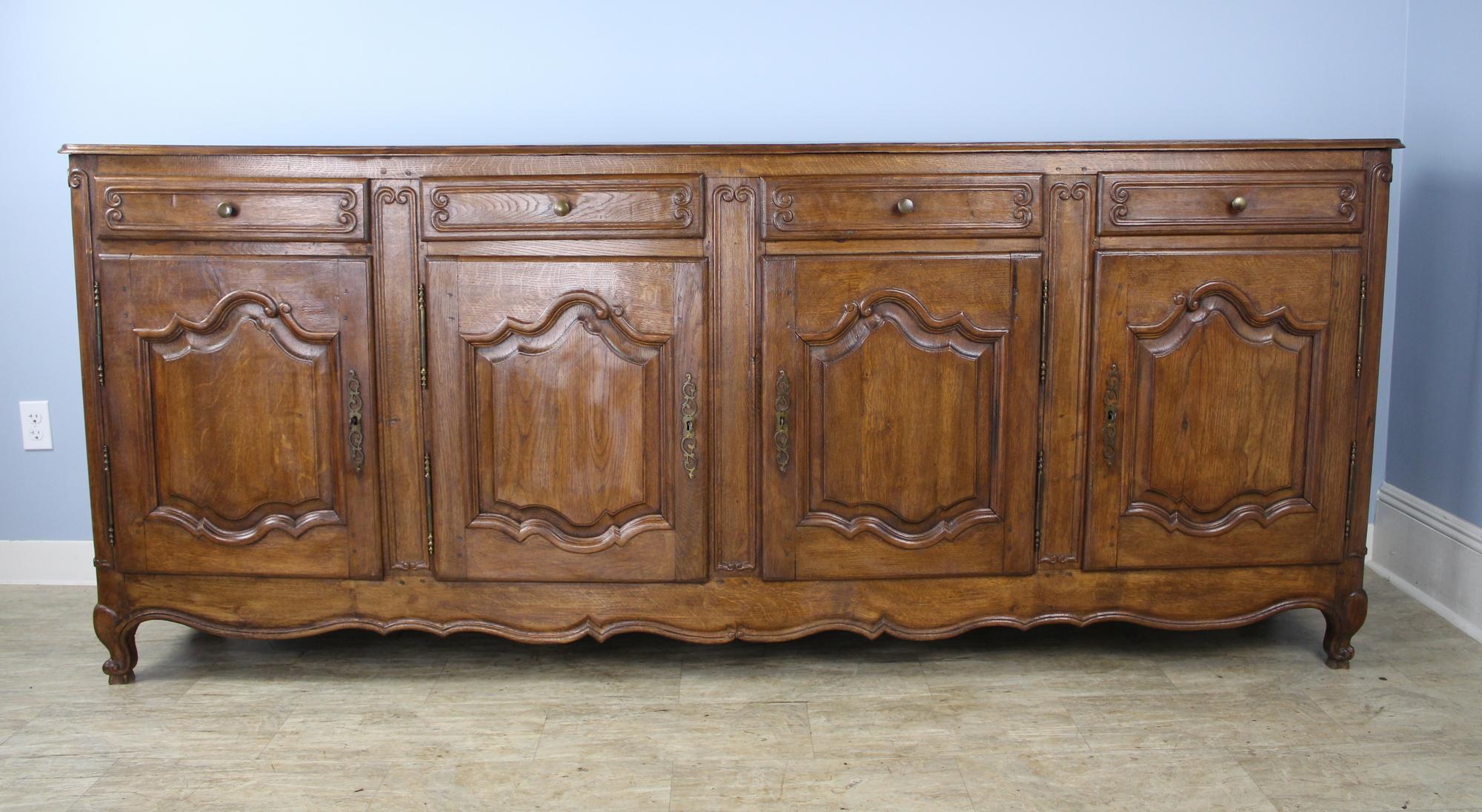 A large French chestnut buffet or enfilade, grand in both scale and sensibility. Carved detail on both the door panels and the drawers and snail feet to complete the look. The interior and the top are both clean and in very good condition. One