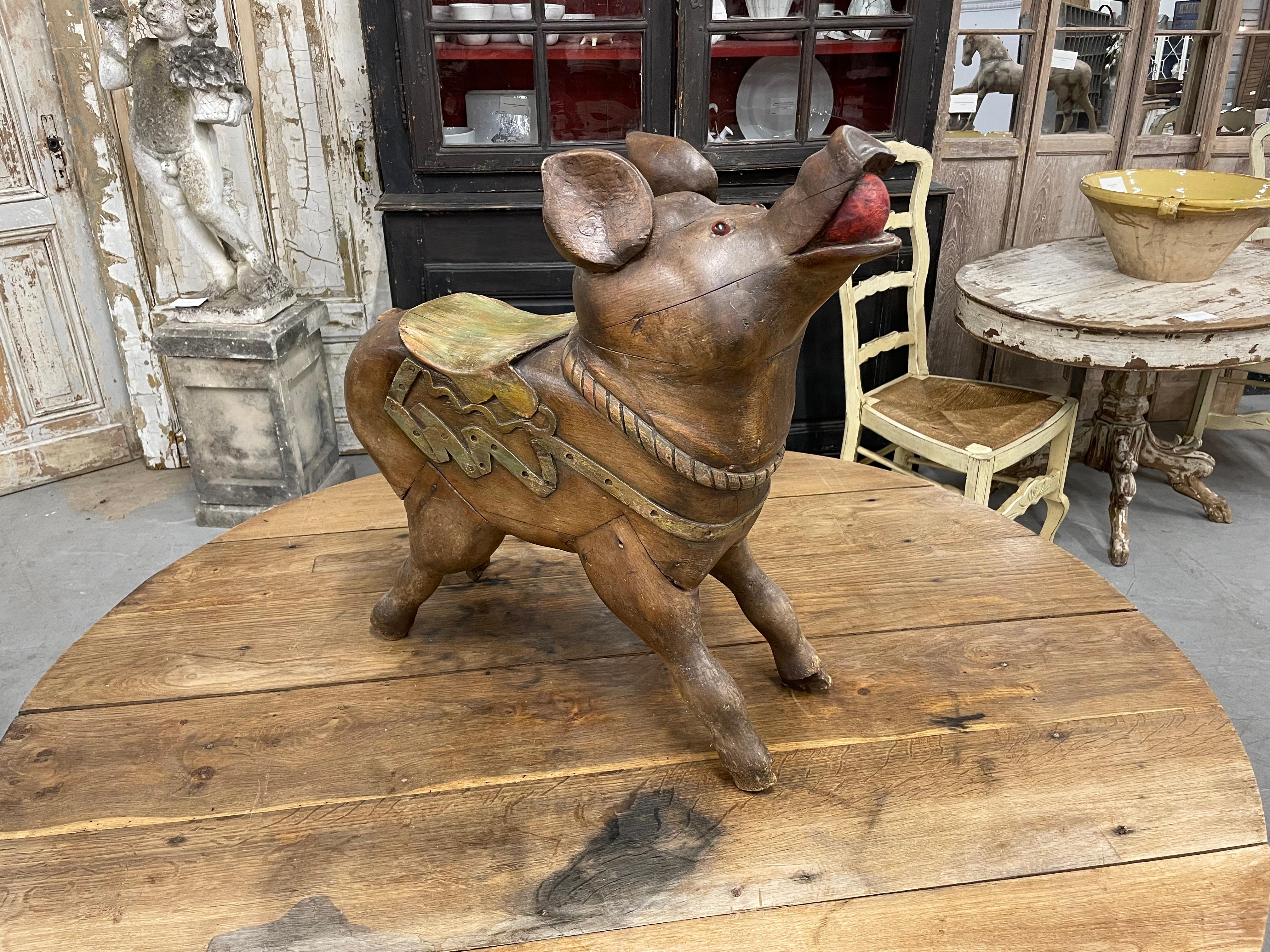 Rare antique French hand carved children's carousel pig or monter le cochon.

This primitive polychromed grunter is full of charm, character and quirkiness with a beautifully carved harness and saddle. A bright red apple is firmly gripped in his