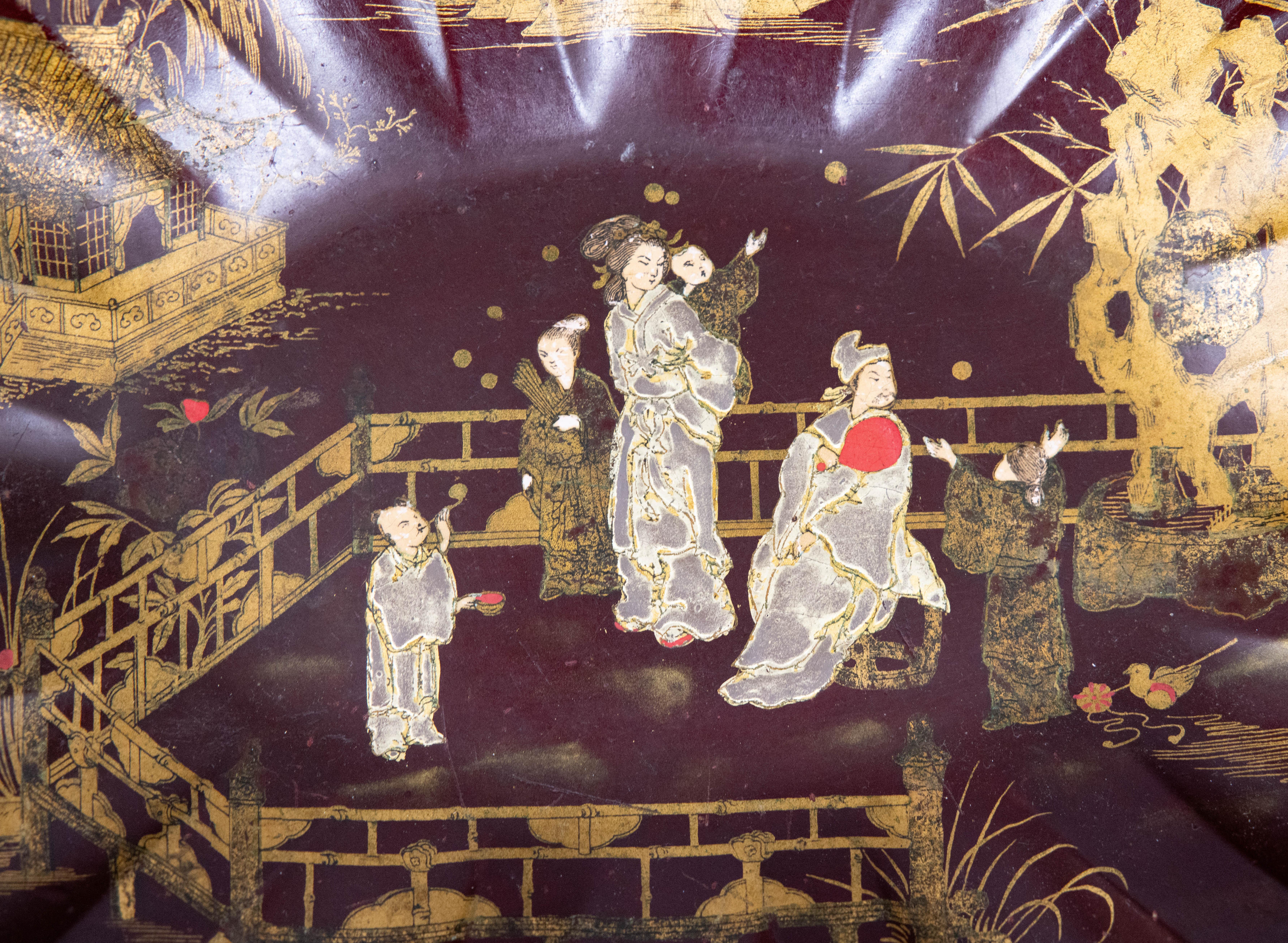 A gorgeous antique 19th-Century French Chinoiserie dark red burgundy papier mache japanned scalloped tray or bowl with an Asian chinoiserie design. This fine tray is hand made depicting a hand painted garden with figures in recreation, pagodas, and