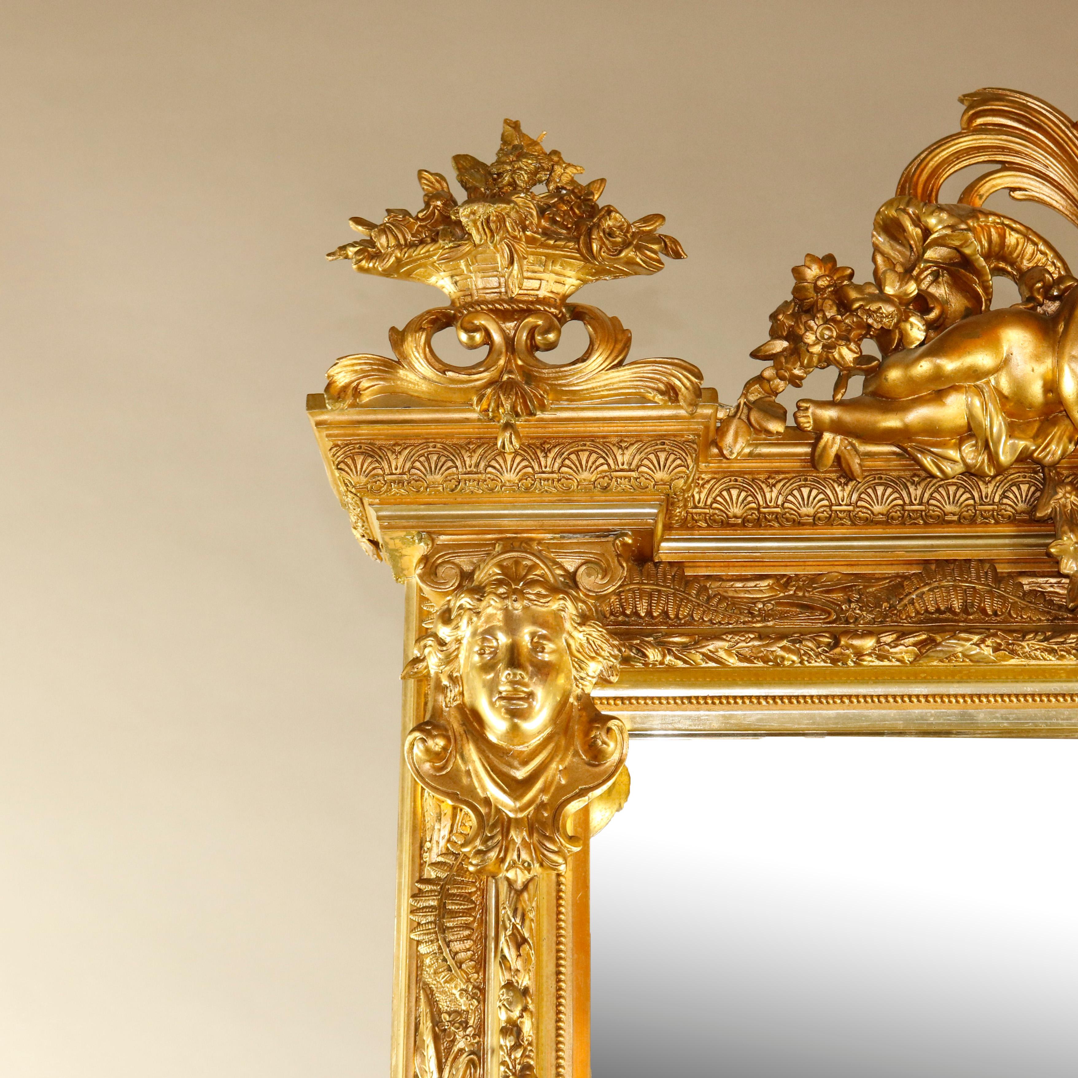 An antique French Baroque style figural pier mirror offers giltwood surround with pierced scroll and foliate crest having central classical female bust flanked by Cherubs and Panier de Fleurs surmounting fern and foliate decorated frame with
