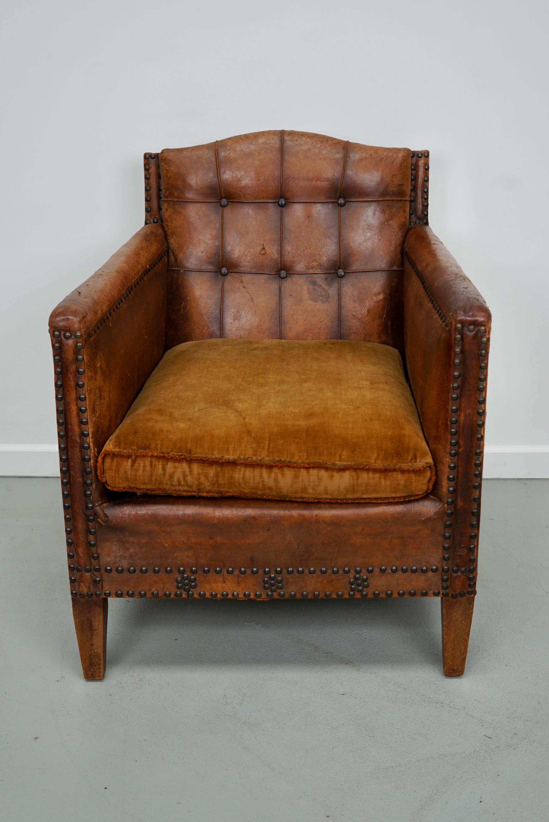 This leather club chair was made in France in the early 20th century. It features a solid wooden frame covered in sheep leather decorated with nails and buttons in the back.