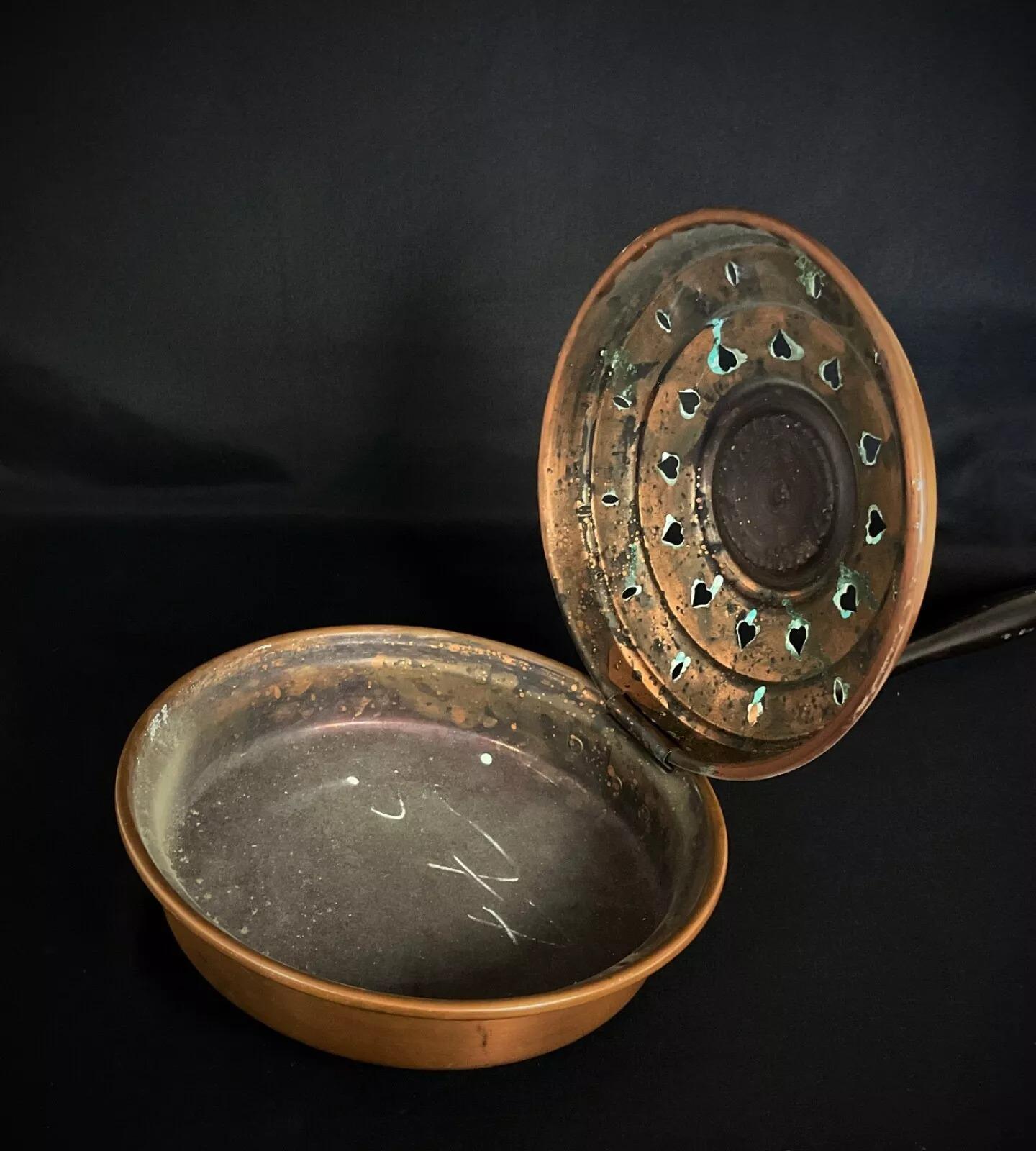This beautiful antique French copper bed warmer from the 20th century features intricate heart motifs on its lid, showcasing a traditional and decorative design. Originally used to warm beds by filling it with embers, it now serves as a charming