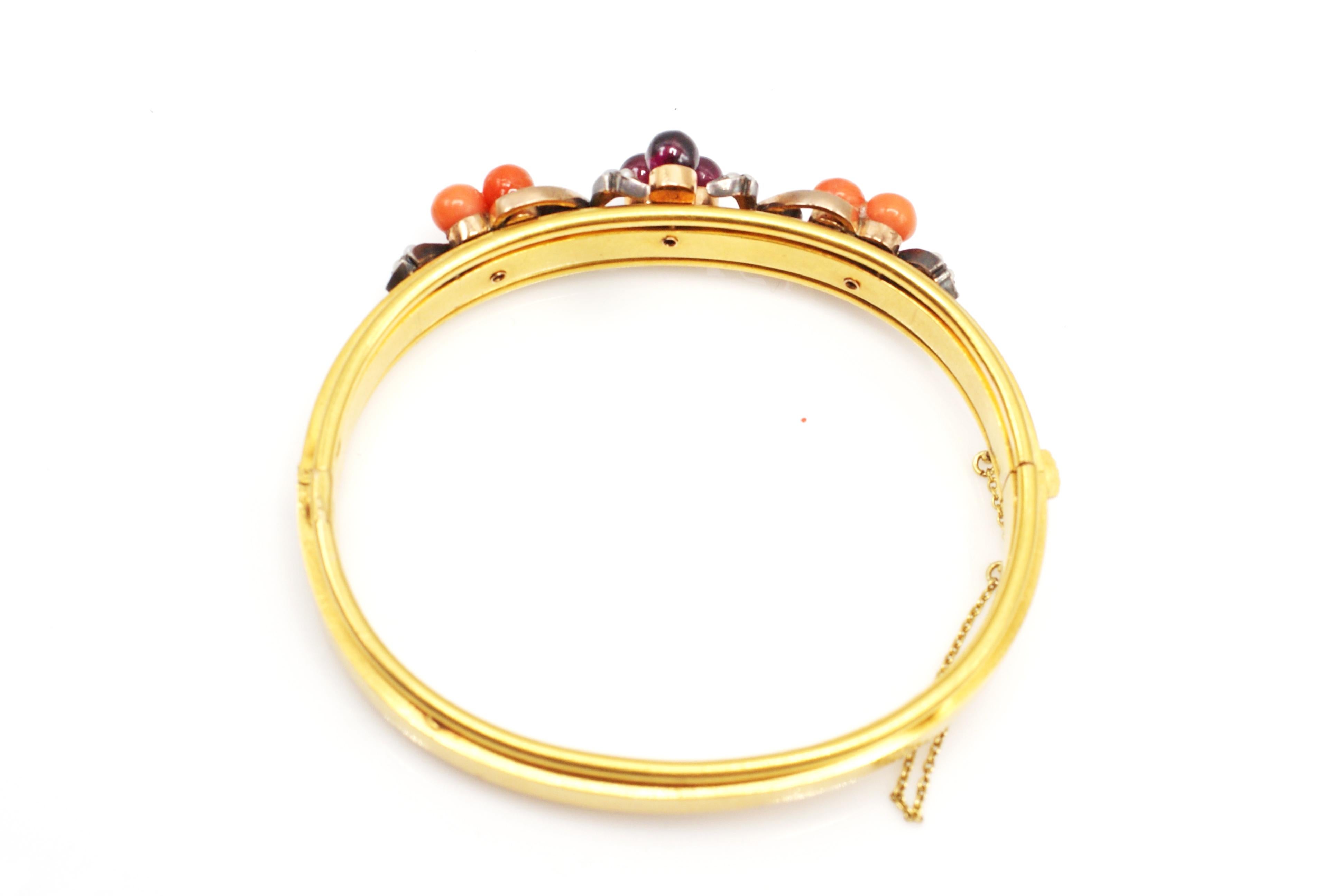 This lovely antique French hinged bangle was masterfully handcrafted in 18 karat yellow gold. 3 round polished burgundy color garnet beads are centrally set with 3 perfectly matched orange-pink coral beads on either side. Set on a gallery of curved
