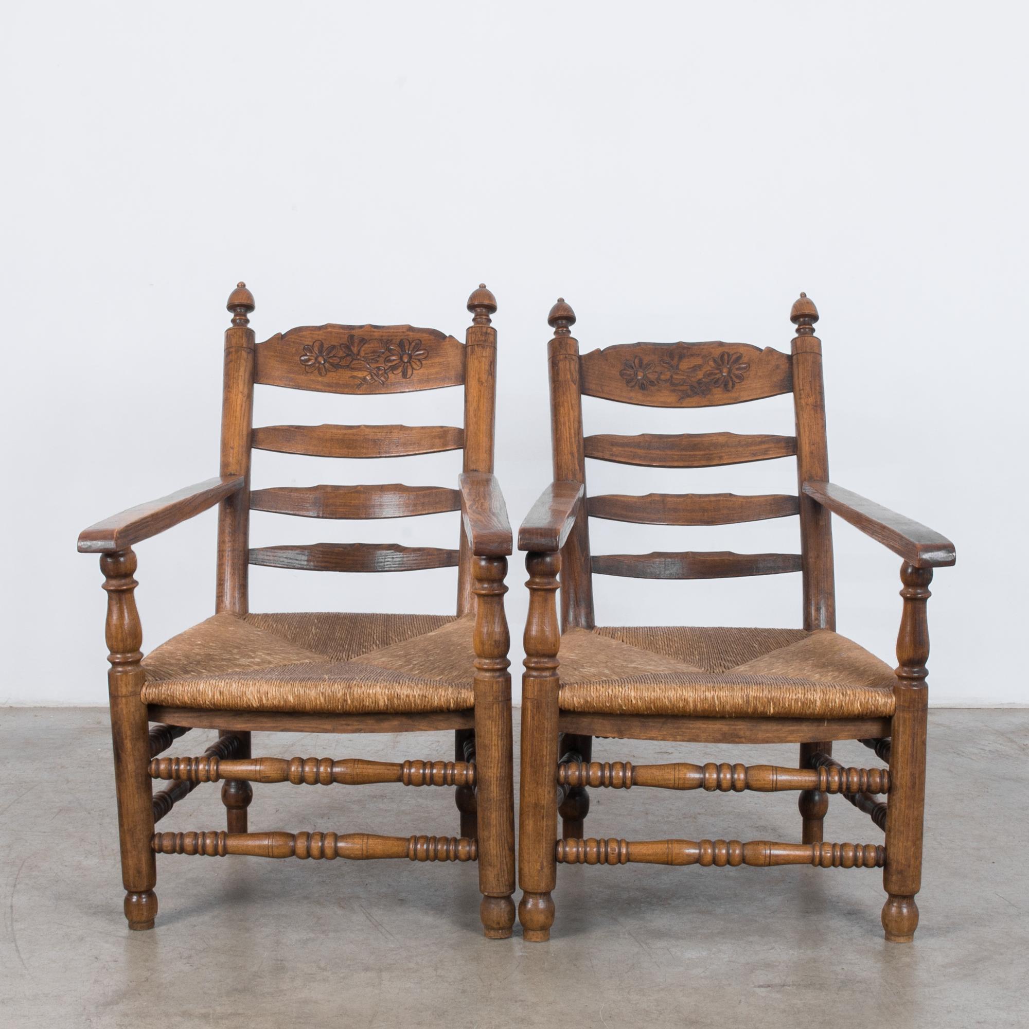 This pair of wooden armchairs with wicker seats and horizontal armrests was made in France, circa 1900. The reclined back comprises four rails with decorative floral carvings on the top rail. The polished wooden frame has a warm character, and the
