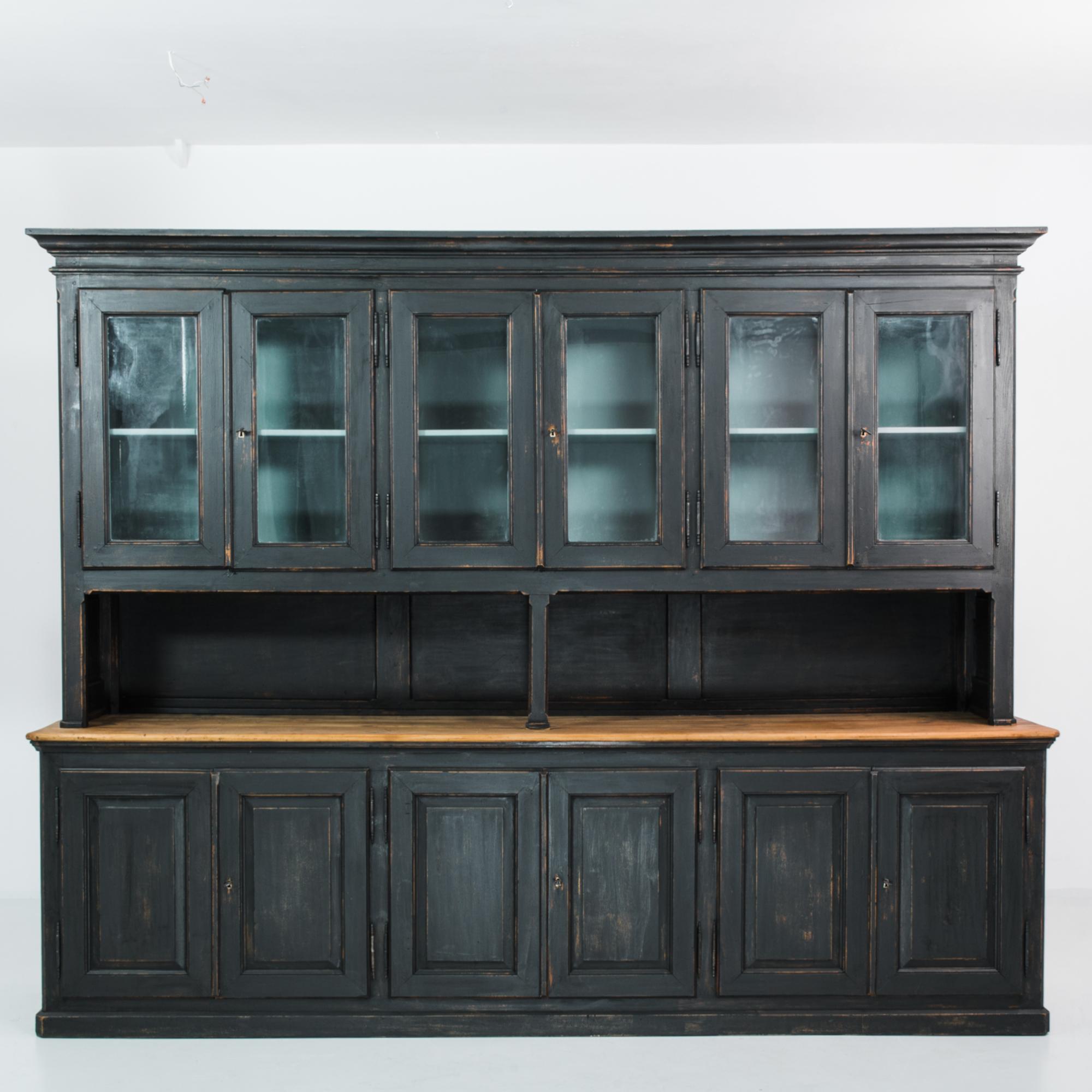 A wood vitrine from France, produced circa 1900. A grand, black patinated wooden buffet cabinet, featuring three glass front, double door upper cabinets, a matching trio of lower wood door double cabinets, and a central shelf. From the blue interior