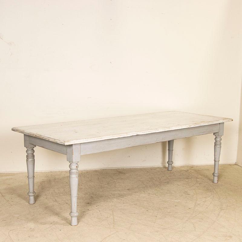 The charm of this French country farm table comes from the simple lines, turned legs and gently aged painted finish. The base still maintains its gray paint which is complimented by the contrasting white painted top. Note in photos how the paint and
